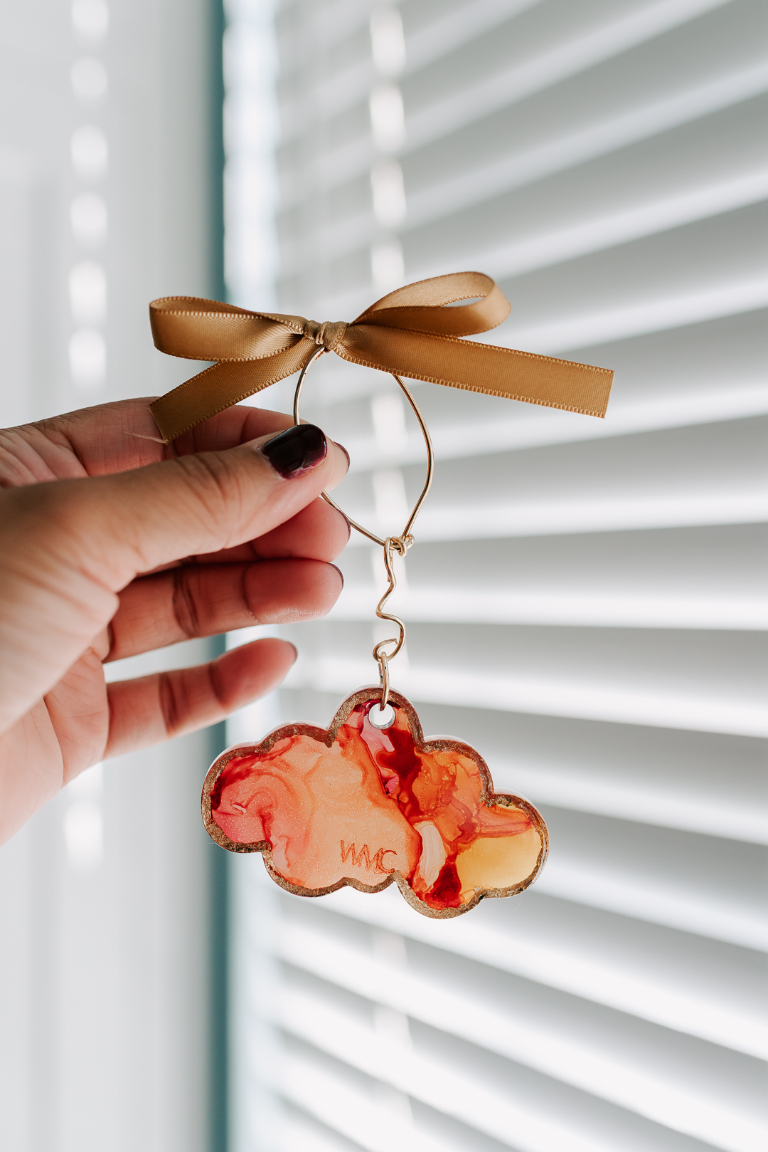 Hand holding a cloud-shaped ornament with a ribbon, in front of window blinds.