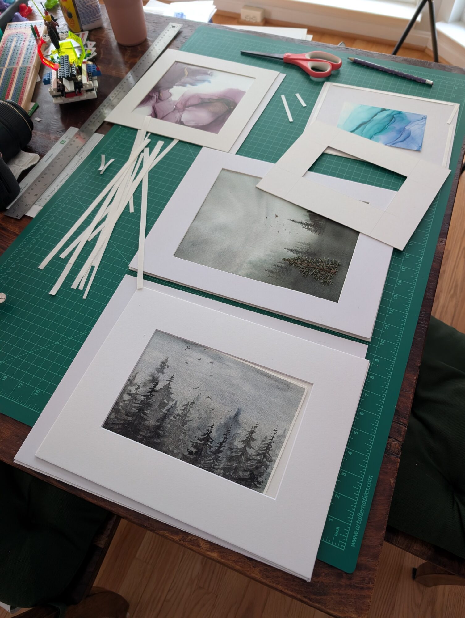 Photographs and picture frames on a green cutting mat with scissors and tools nearby, on a wooden table.