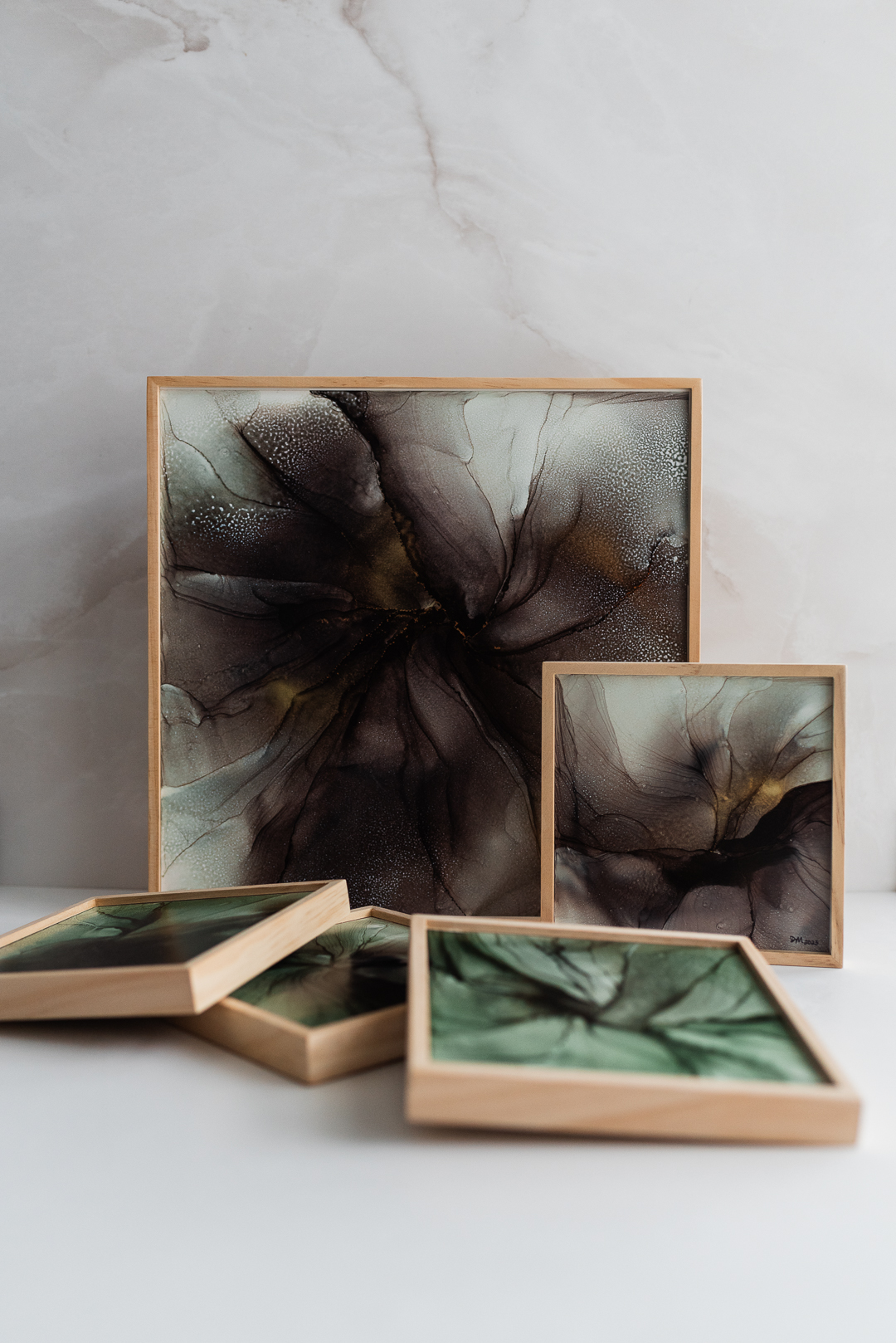 Set of five framed abstract art pieces with dark, swirling patterns, arranged on a white surface against a light gray wall.