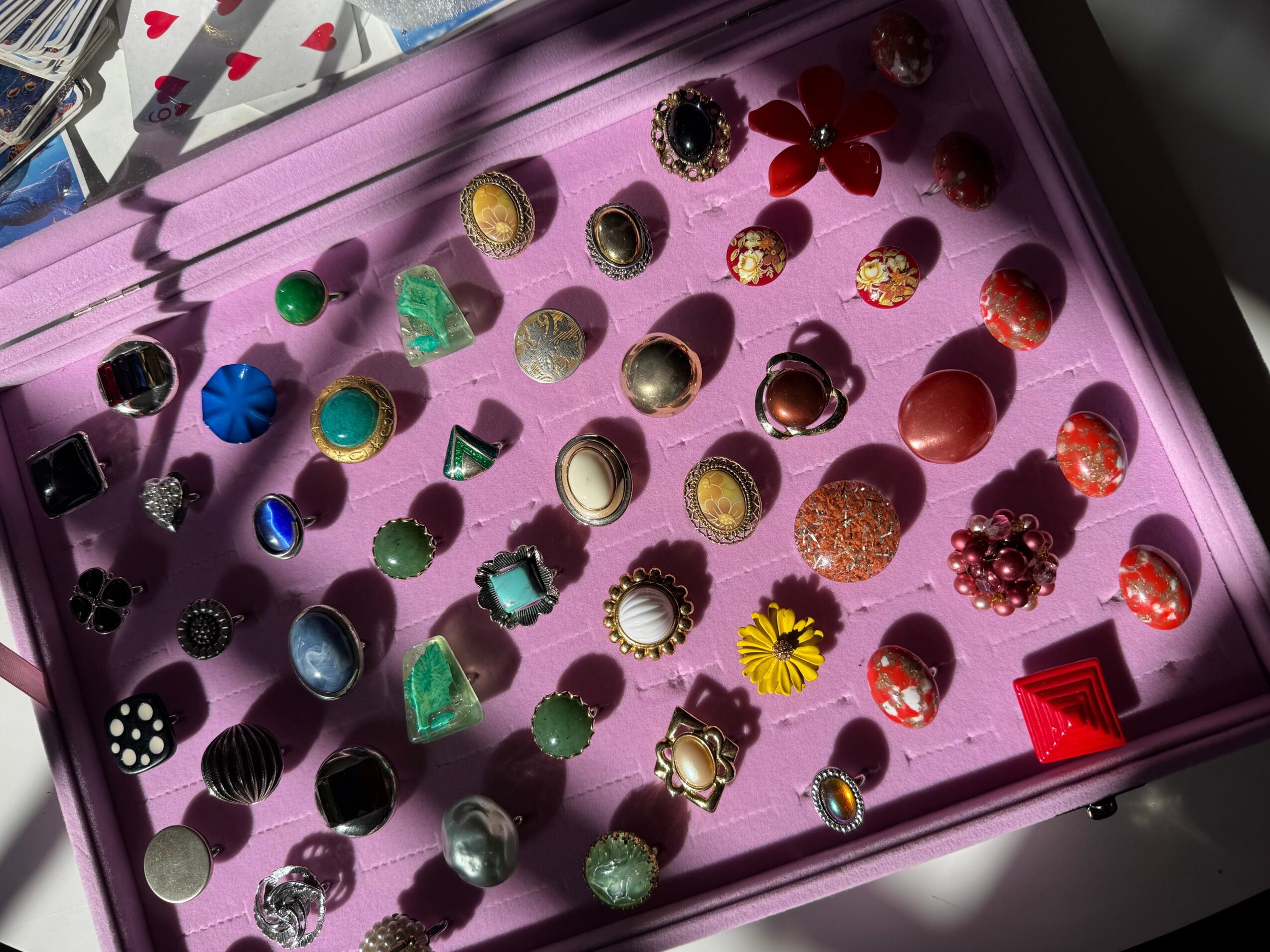 Pink tray with various colorful earrings and jewelry pieces arranged in rows.