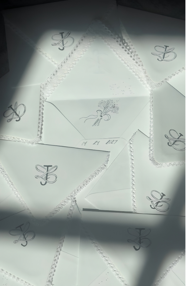Multiple white envelopes with black decorative initials and a bow design, arranged on a surface.