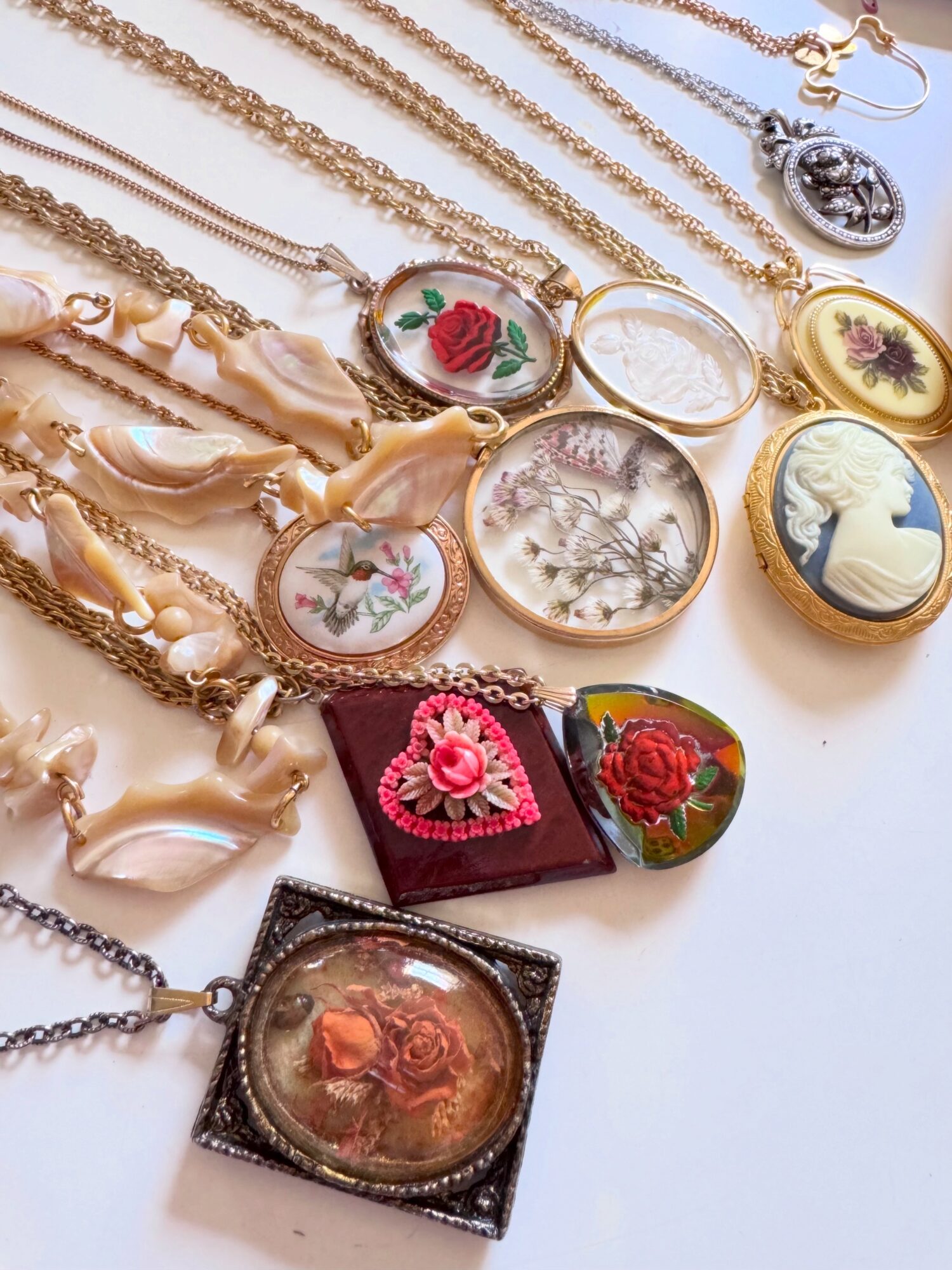 Collection of necklaces and jewelry with various pendants, including floral and cameo designs, arranged on a white surface.