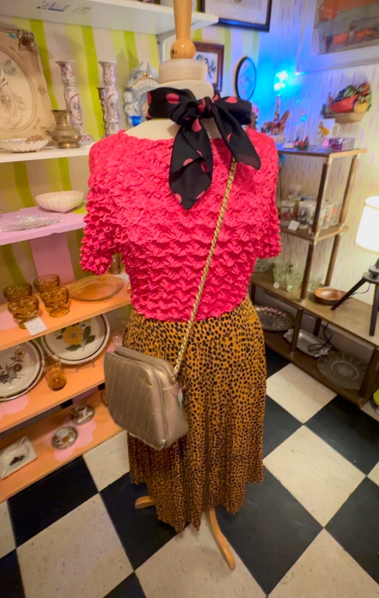 Mannequin dressed in a pink textured top, leopard print skirt, black and pink scarf, and gray handbag, in a vintage shop.