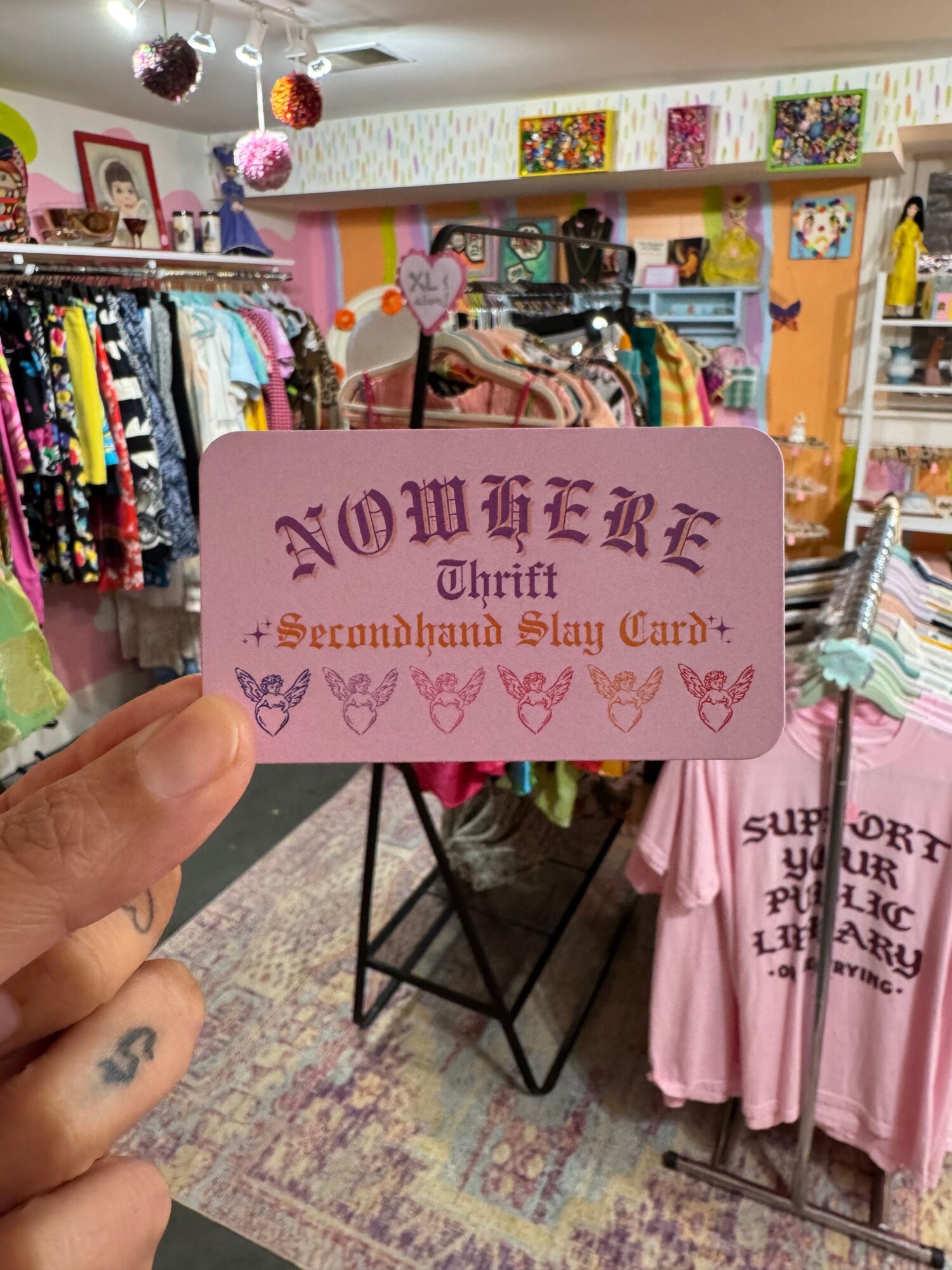Person holding a pink sign with text and hearts in a clothing store, with racks of clothes in the background.