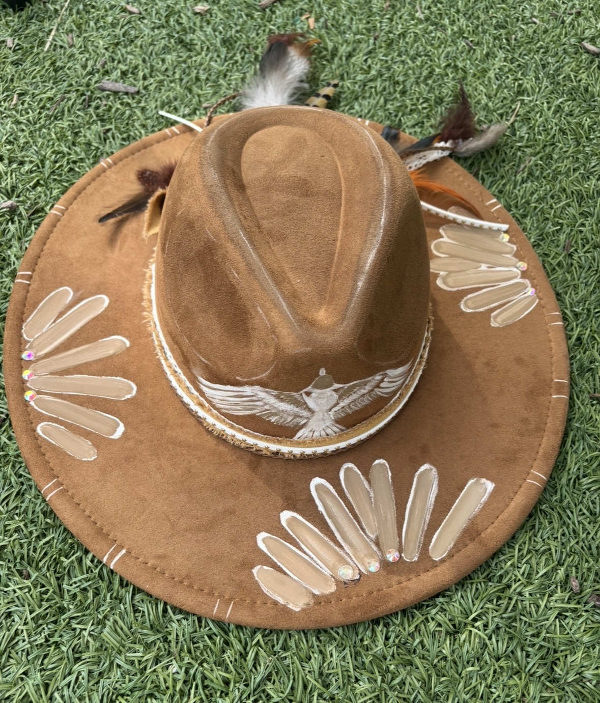 Brown leather hat with feather accents and pale decorative stitching on green grass.