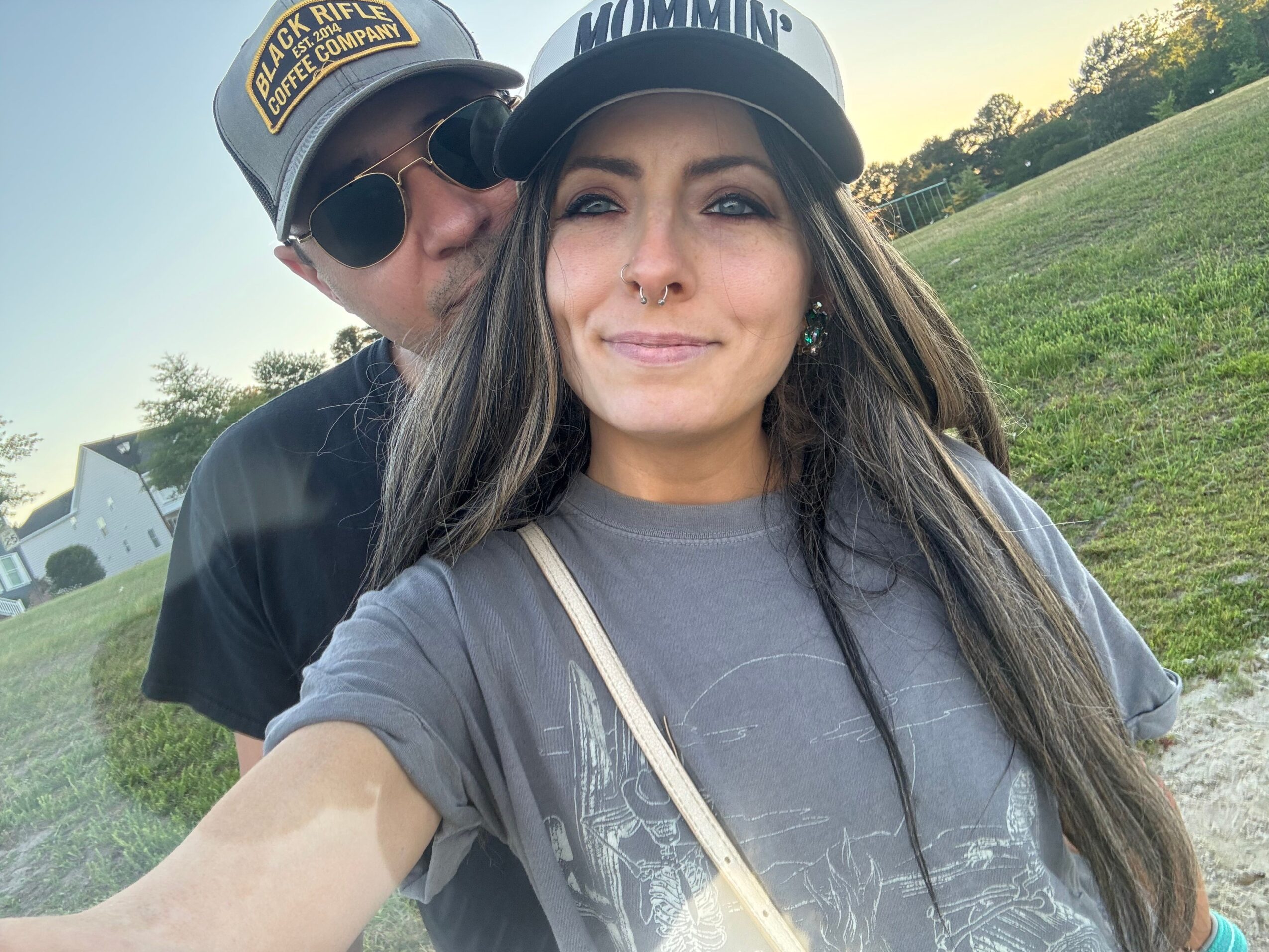 Two people wearing helmets sit outdoors beside a grassy area.