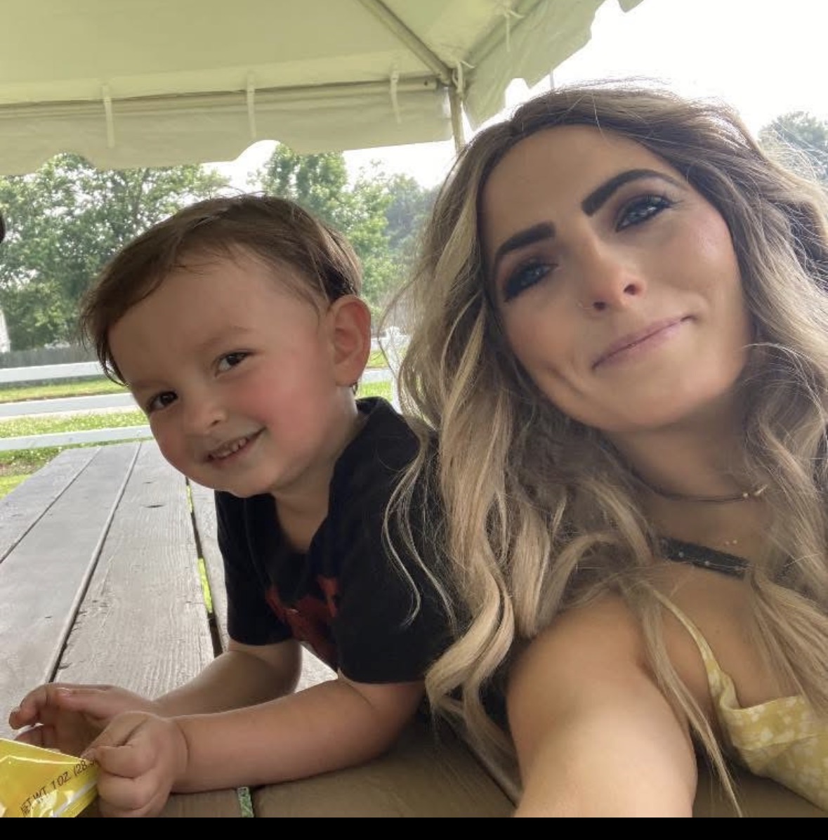 A woman and a young child lean together at a picnic table beneath a canopy.