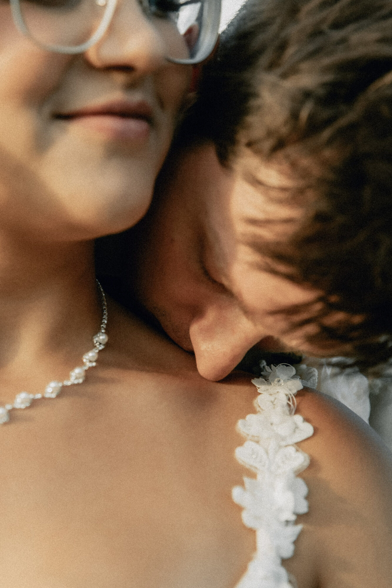 Close-up of two people, one with glasses and a necklace, the other resting their head on the shoulder, with floral details on clothing.