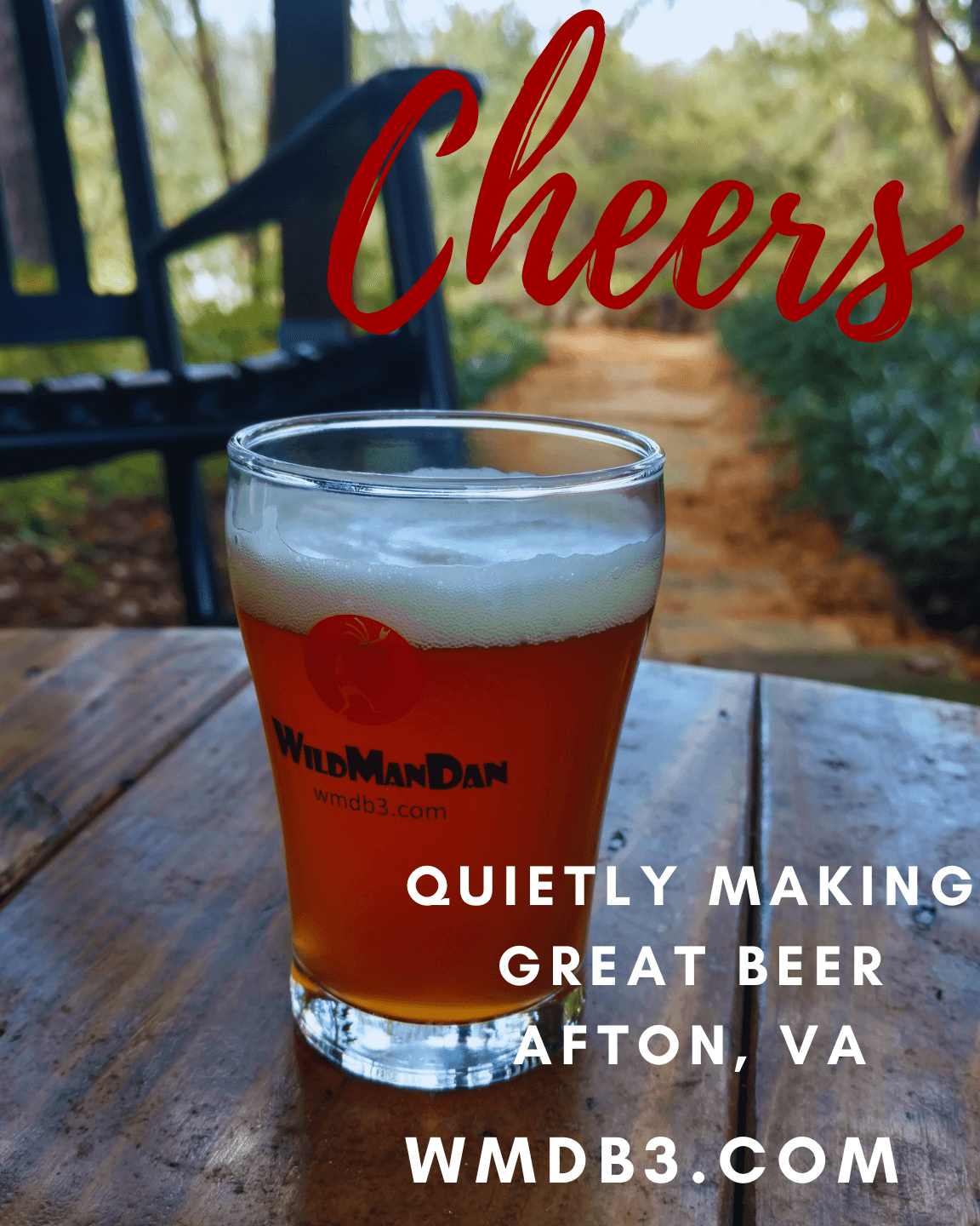 A glass of beer on a wooden table outdoors with trees in the background, and the word 'Cheers' in red script above.