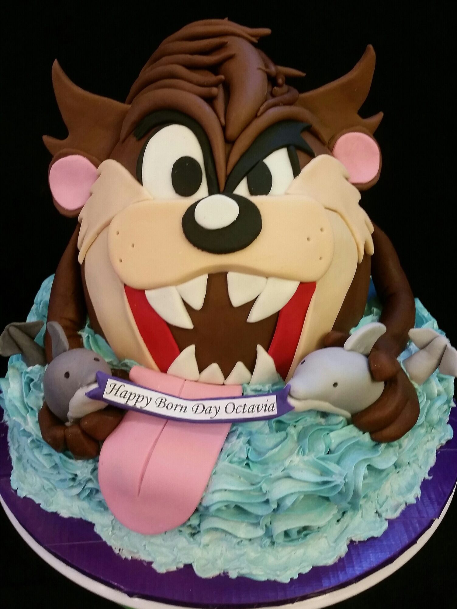 Cake shaped like a cartoon cat with large eyes, pink cheeks, and a big open mouth, surrounded by blue frosting and small mice.