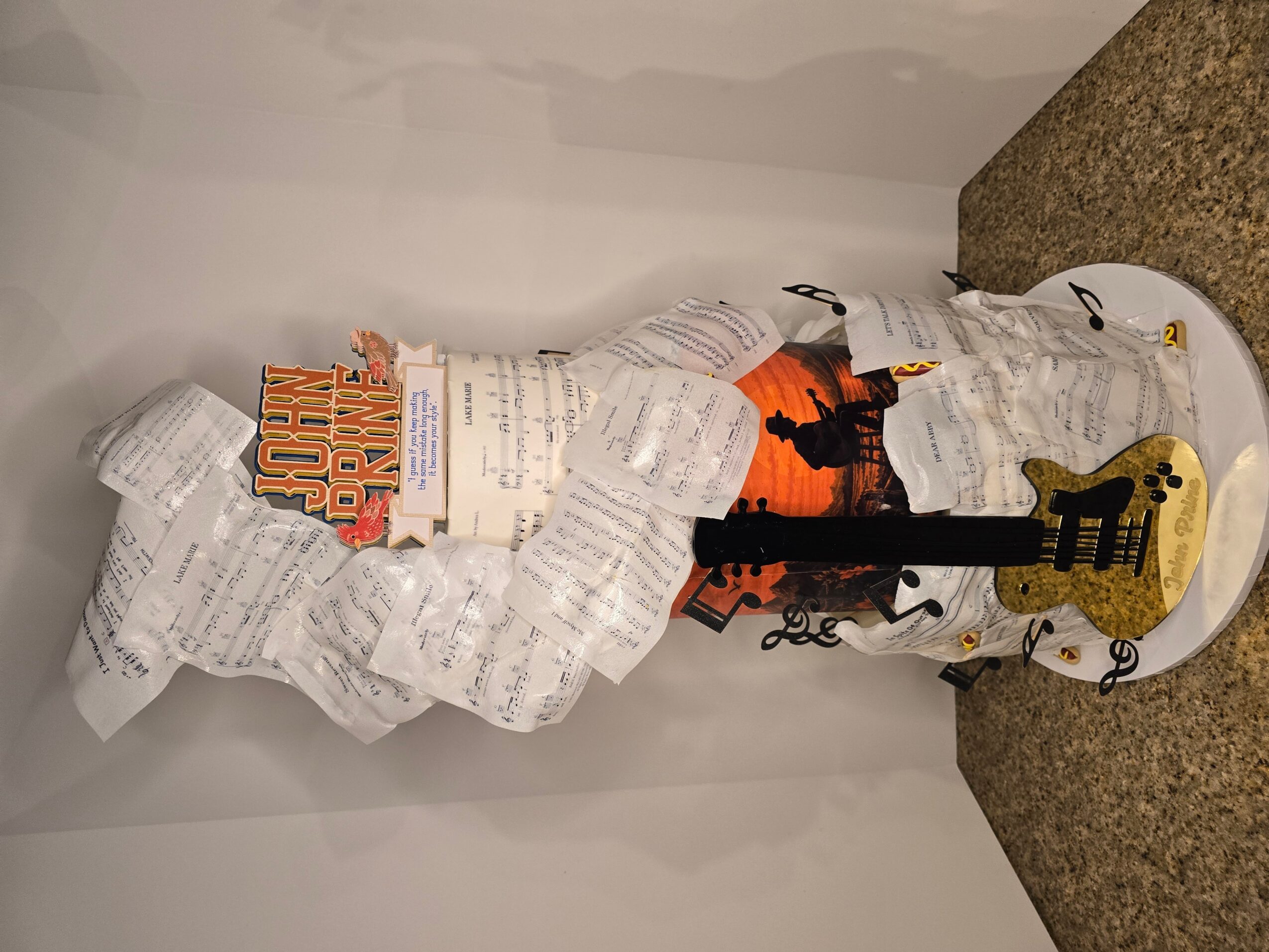 A guitar-shaped object covered with crumpled receipts and papers, placed on a countertop against a white wall.