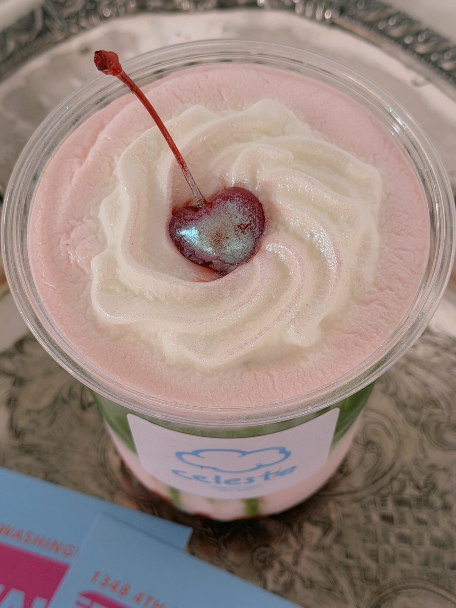 A cup of pink and white soft serve ice cream with a cherry on top, placed on a table.