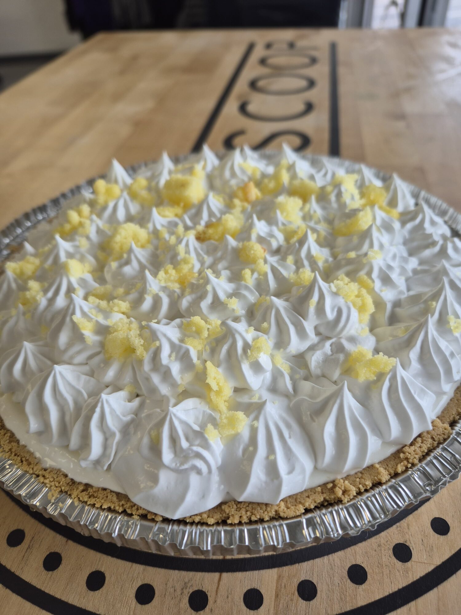 Lemon meringue pie with whipped topping and lemon pieces on a silver tray, on a wooden table.