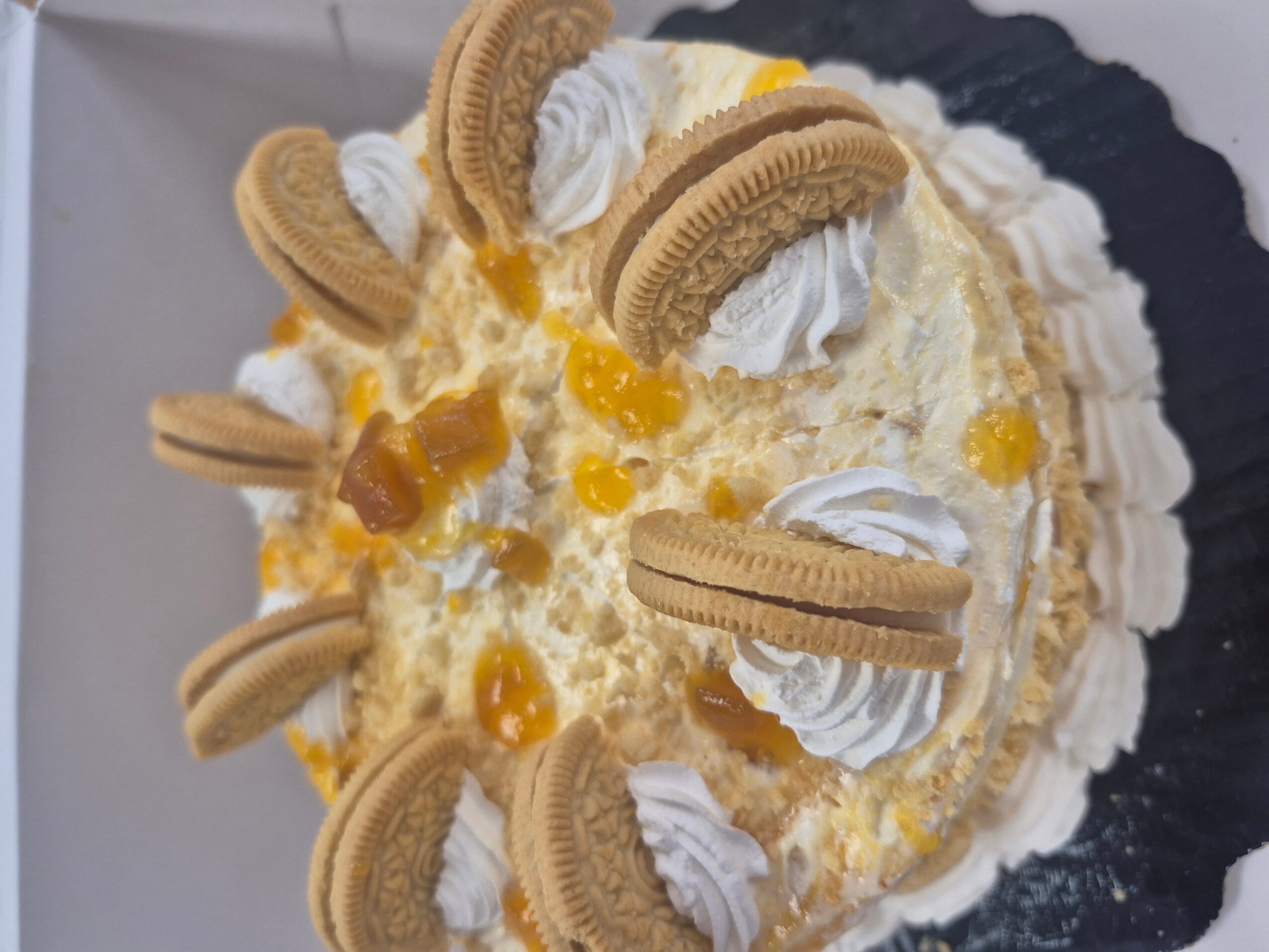Cake decorated with Oreo cookies, whipped cream, and yellow topping, on a black plate.