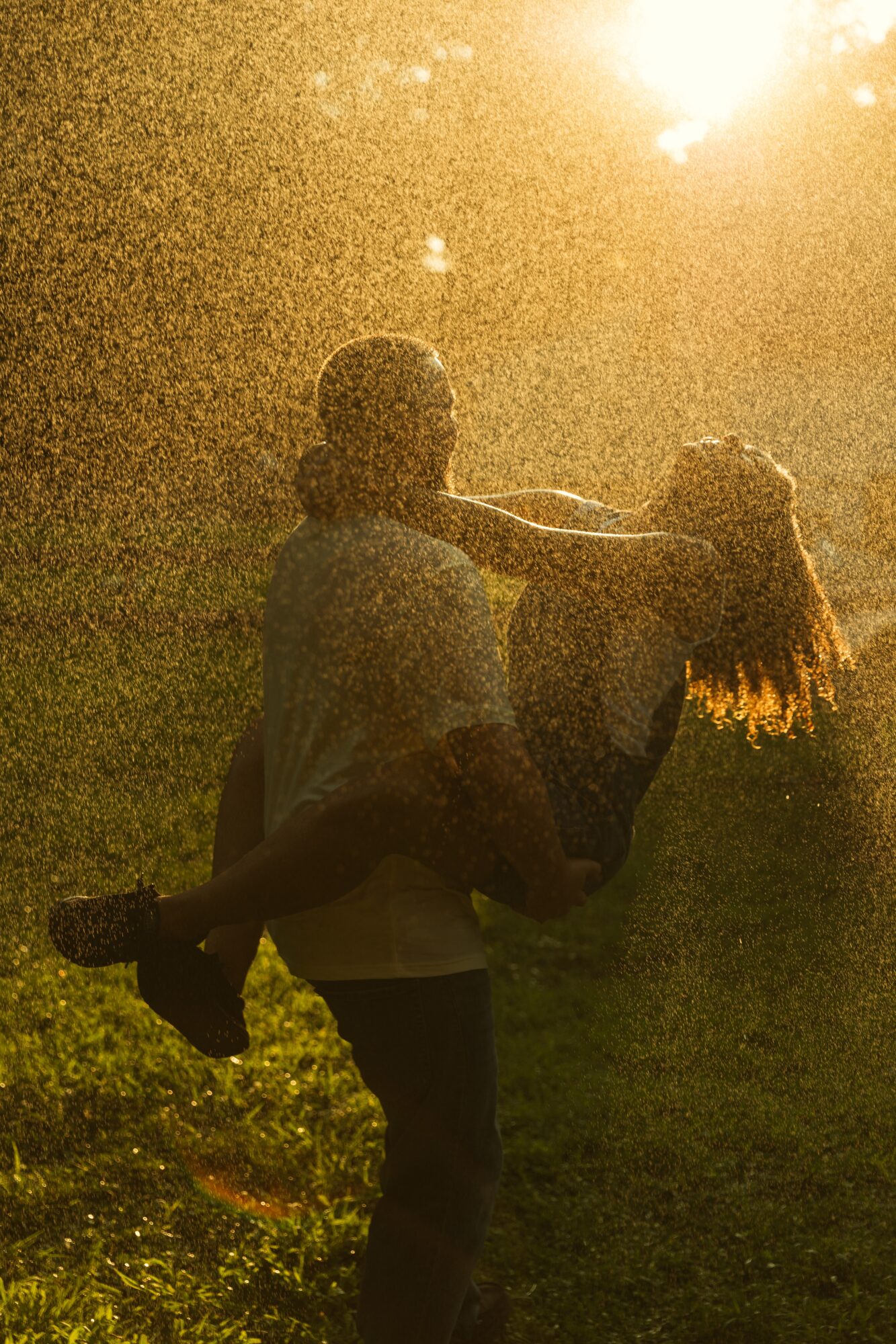 Two children playing outdoors at sunset, one lifting the other, with sunlight in the background.