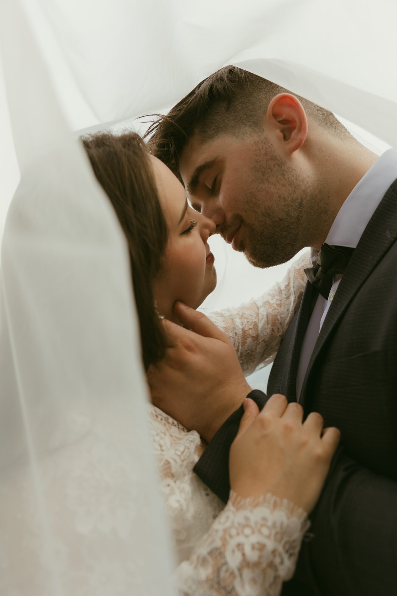 A couple with closed eyes and foreheads touching, embracing closely, with soft white fabric surrounding them.