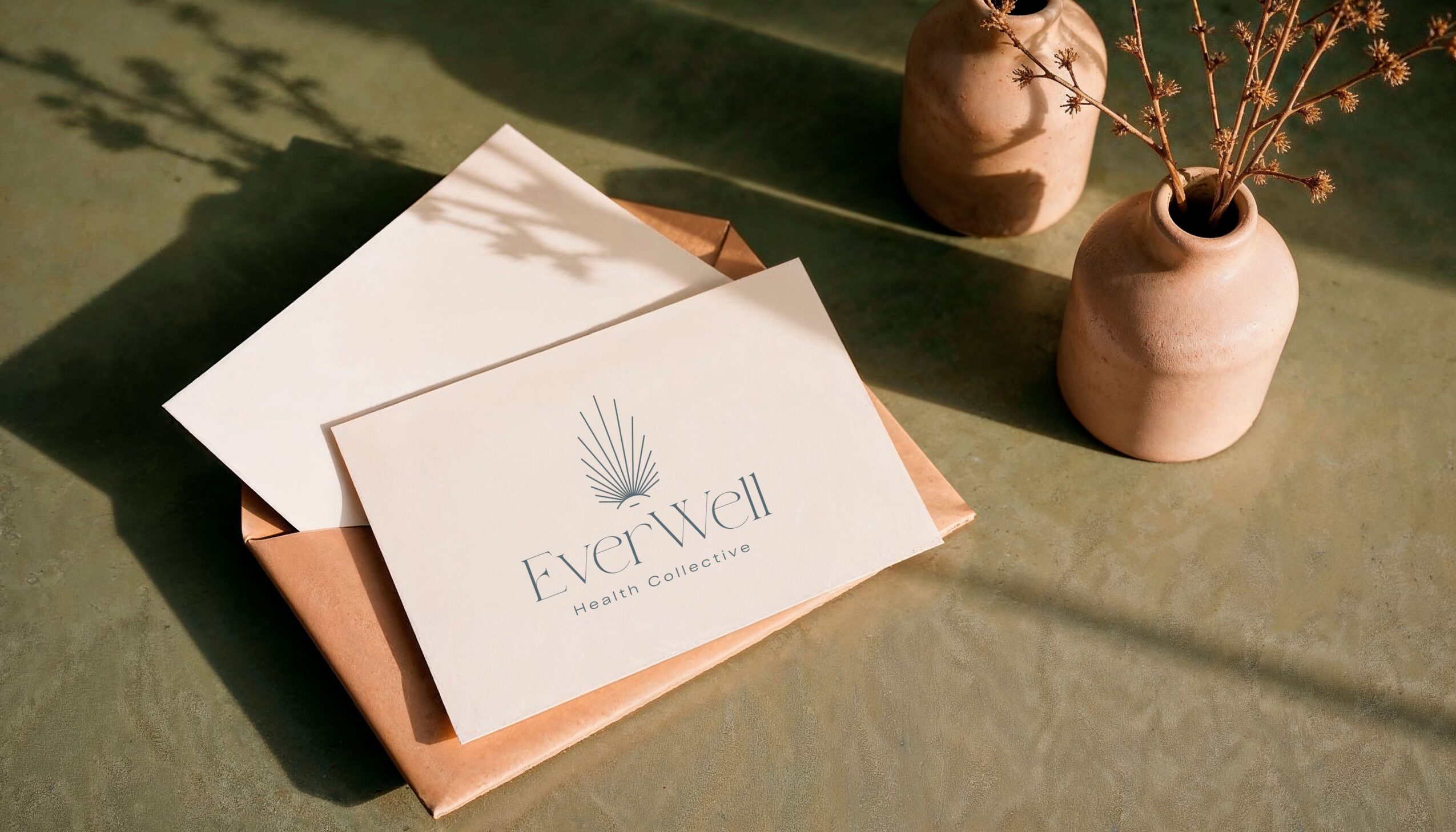 A white card with a palm leaf logo and text, placed on a brown paper package, with two vases containing dried flowers nearby.