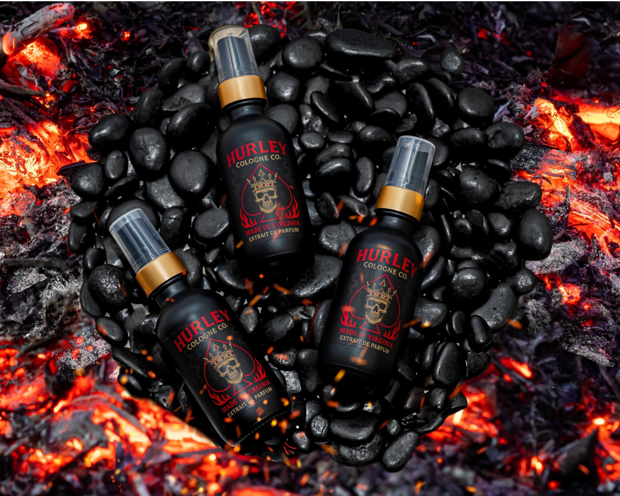 Three black bottles with gold caps on black stones with glowing red and orange embers around them.