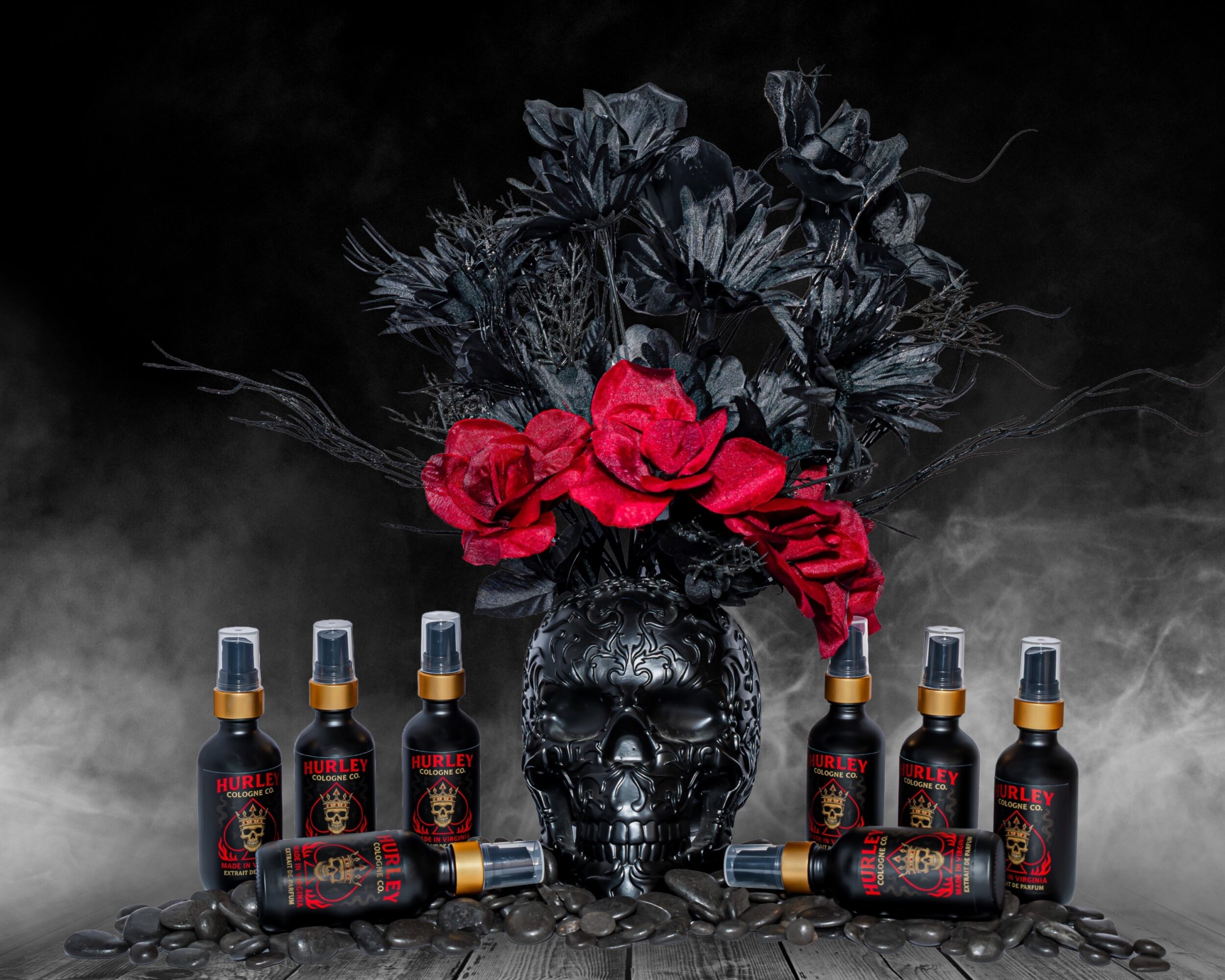 Black skull with red roses and black foliage in a vase, surrounded by small bottles on a dark surface.
