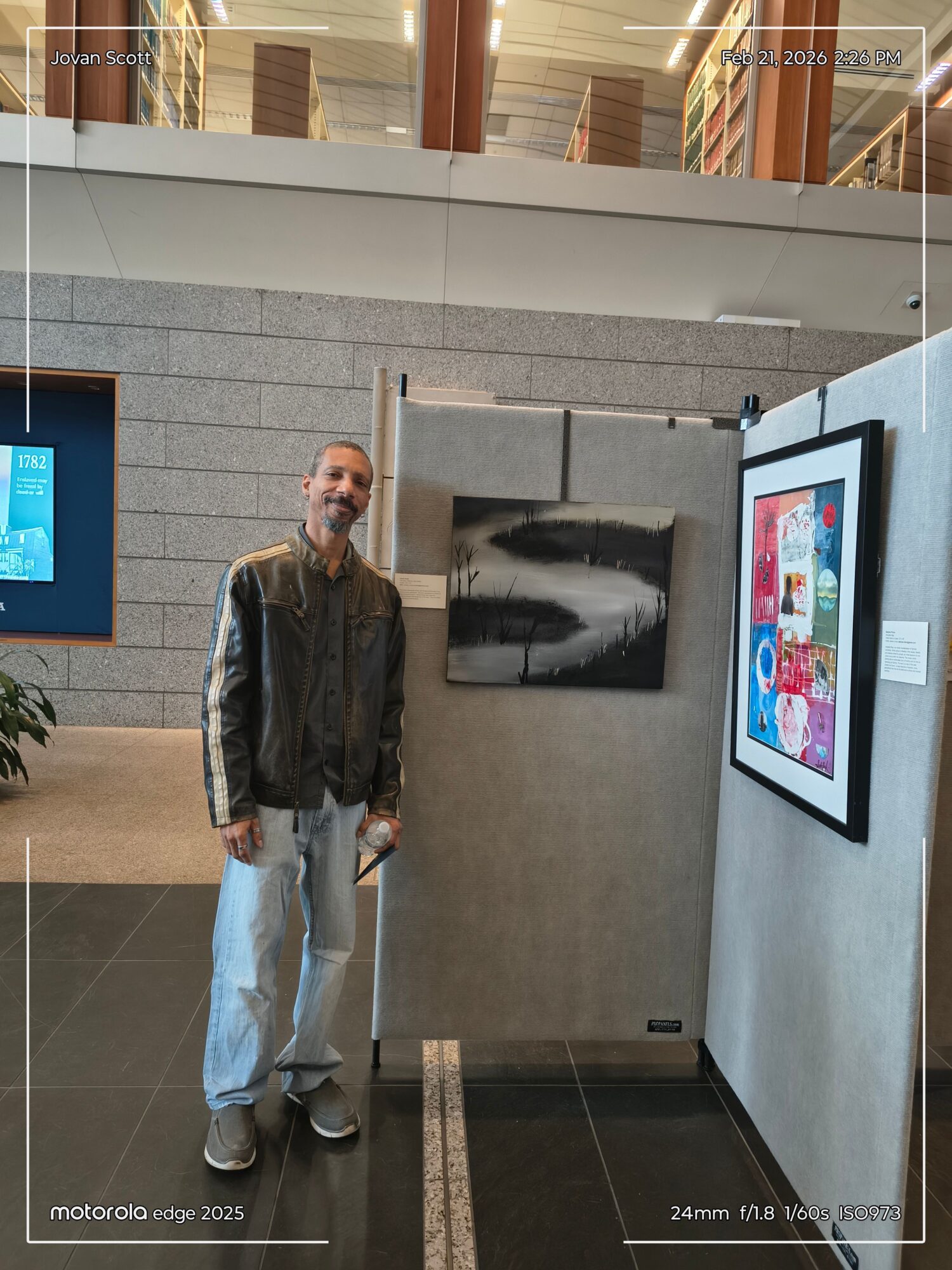 Person standing in front of digital screens in an indoor space, with a gray wall and a small painting behind them.