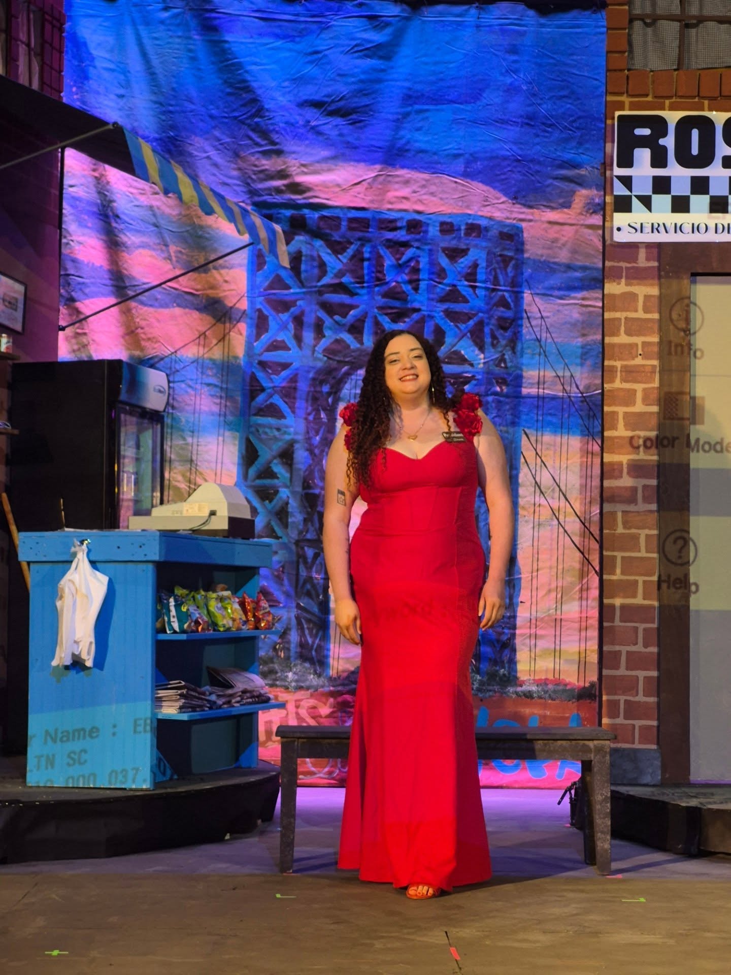 Woman in red dress standing on stage with colorful backdrop and set pieces.
