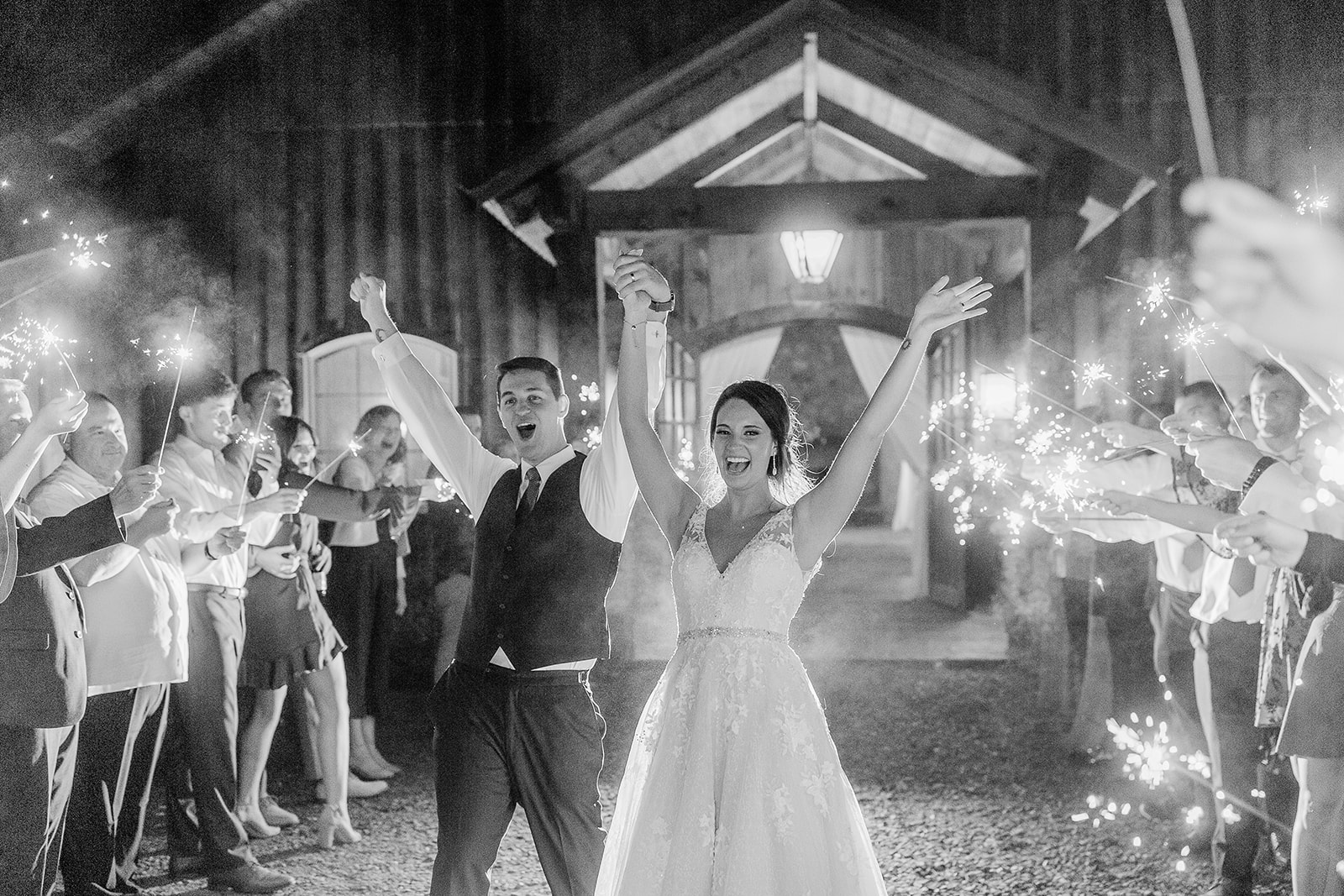 People celebrating with sparklers outside a building at night, some raising their hands, in black and white.