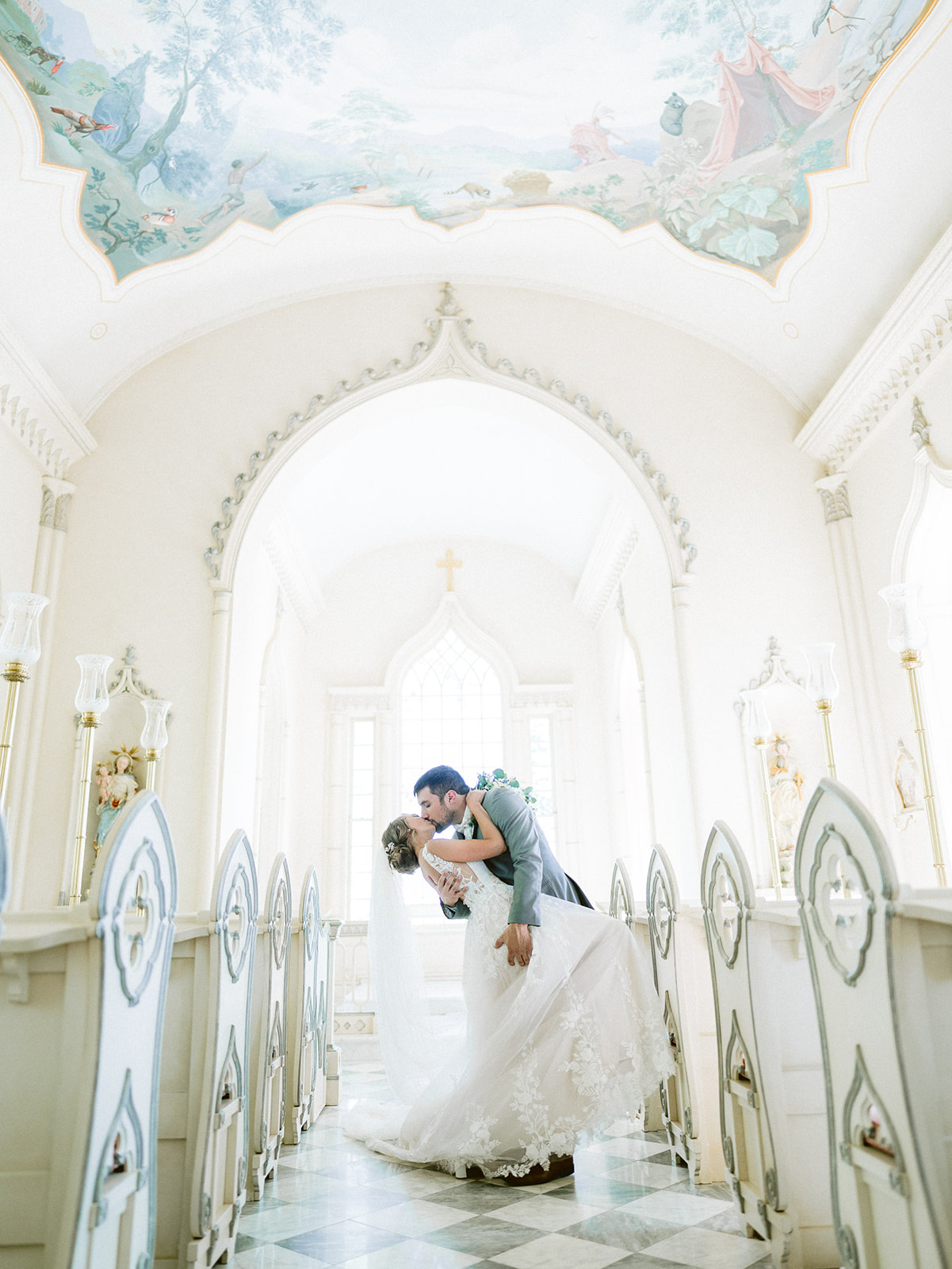 Bride and groom sharing a kiss in a bright, ornate hallway with high ceilings and decorative arches.