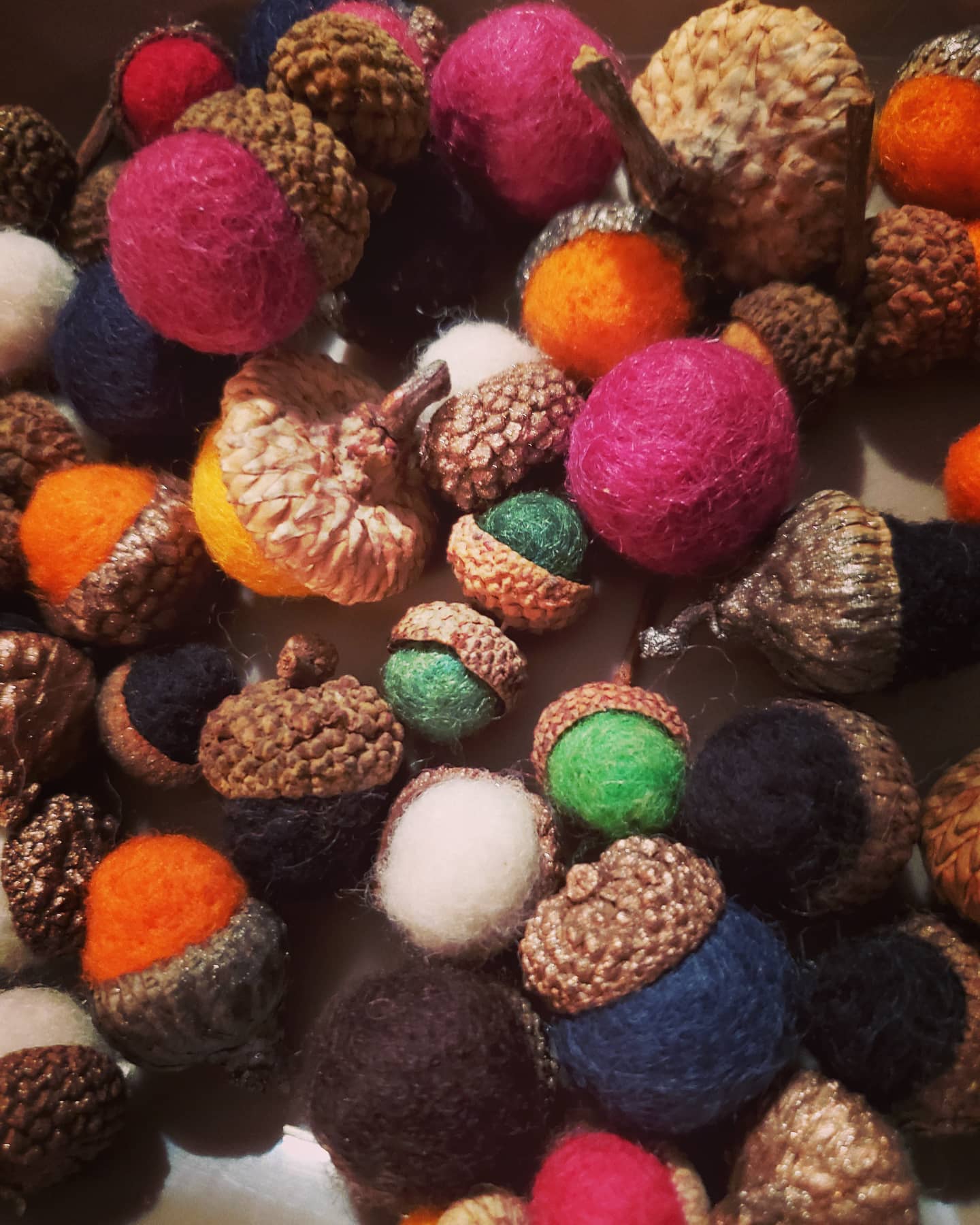 Colorful felted wool balls in various sizes and colors, including pink, orange, white, green, blue, and brown, scattered randomly.
