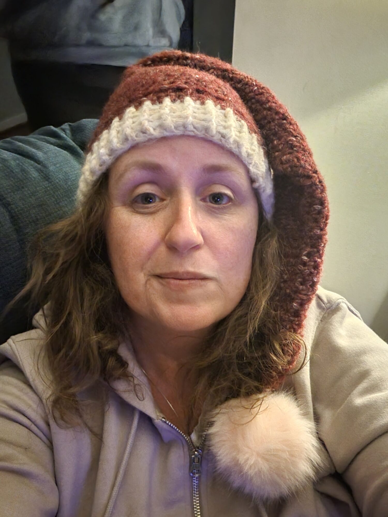 Woman wearing a knit hat with a pom-pom, lying down, looking at the camera, in a cozy setting.
