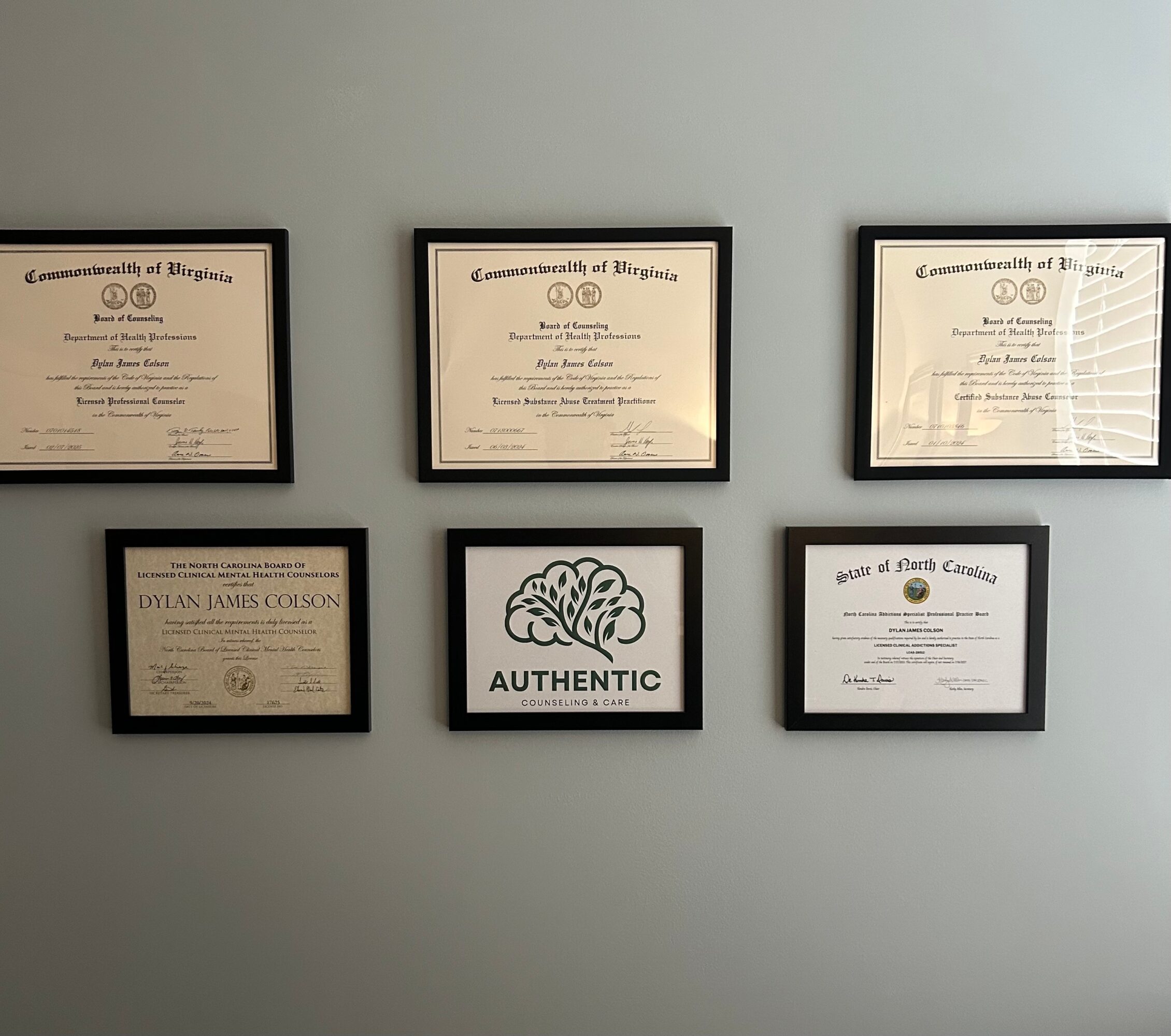 Six framed certificates and a logo with the word 'AUTHENTIC' on a light blue wall.