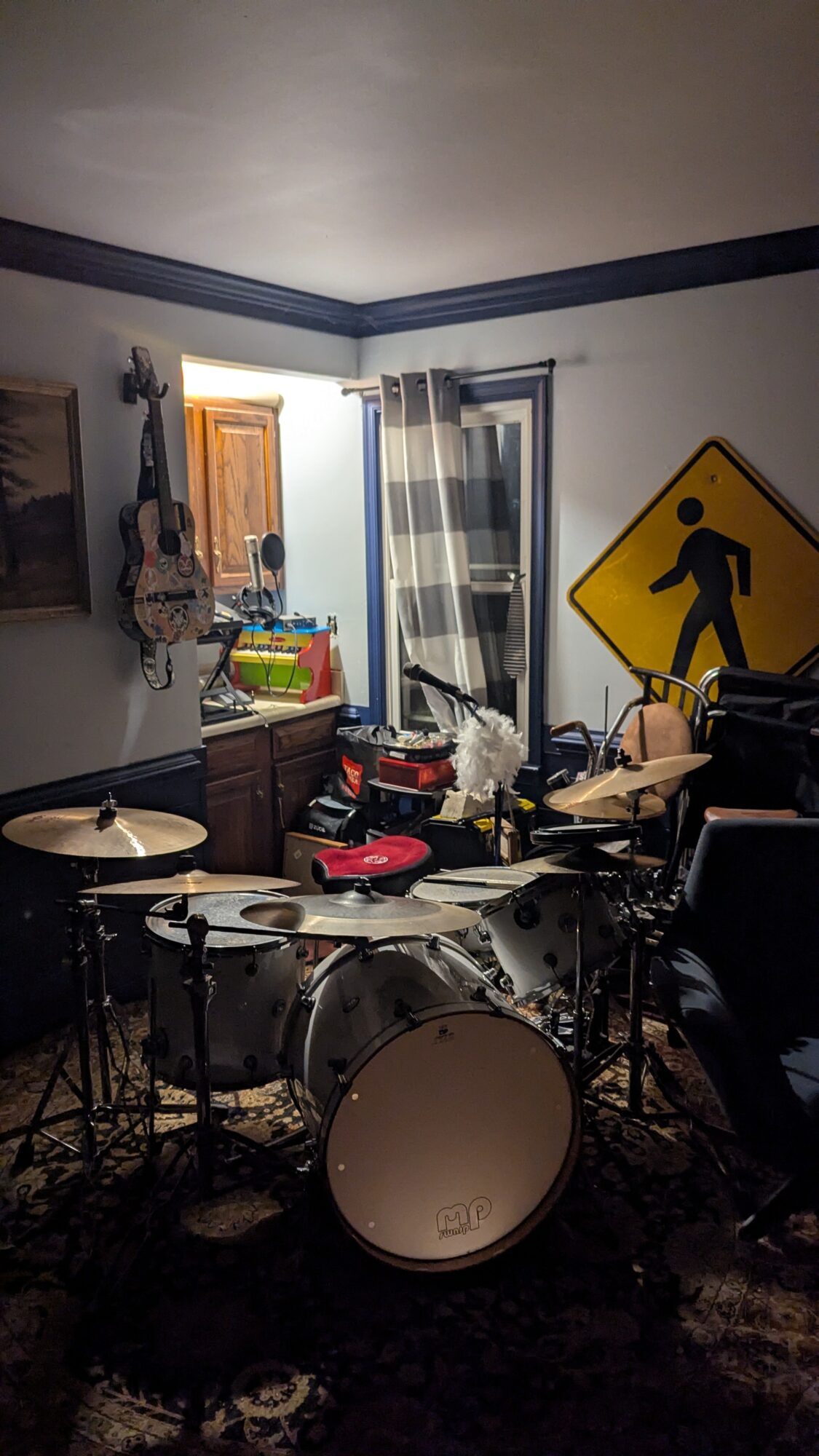 Room with musical instruments, cluttered furniture, and a window with curtains, a yellow pedestrian sign on the wall.