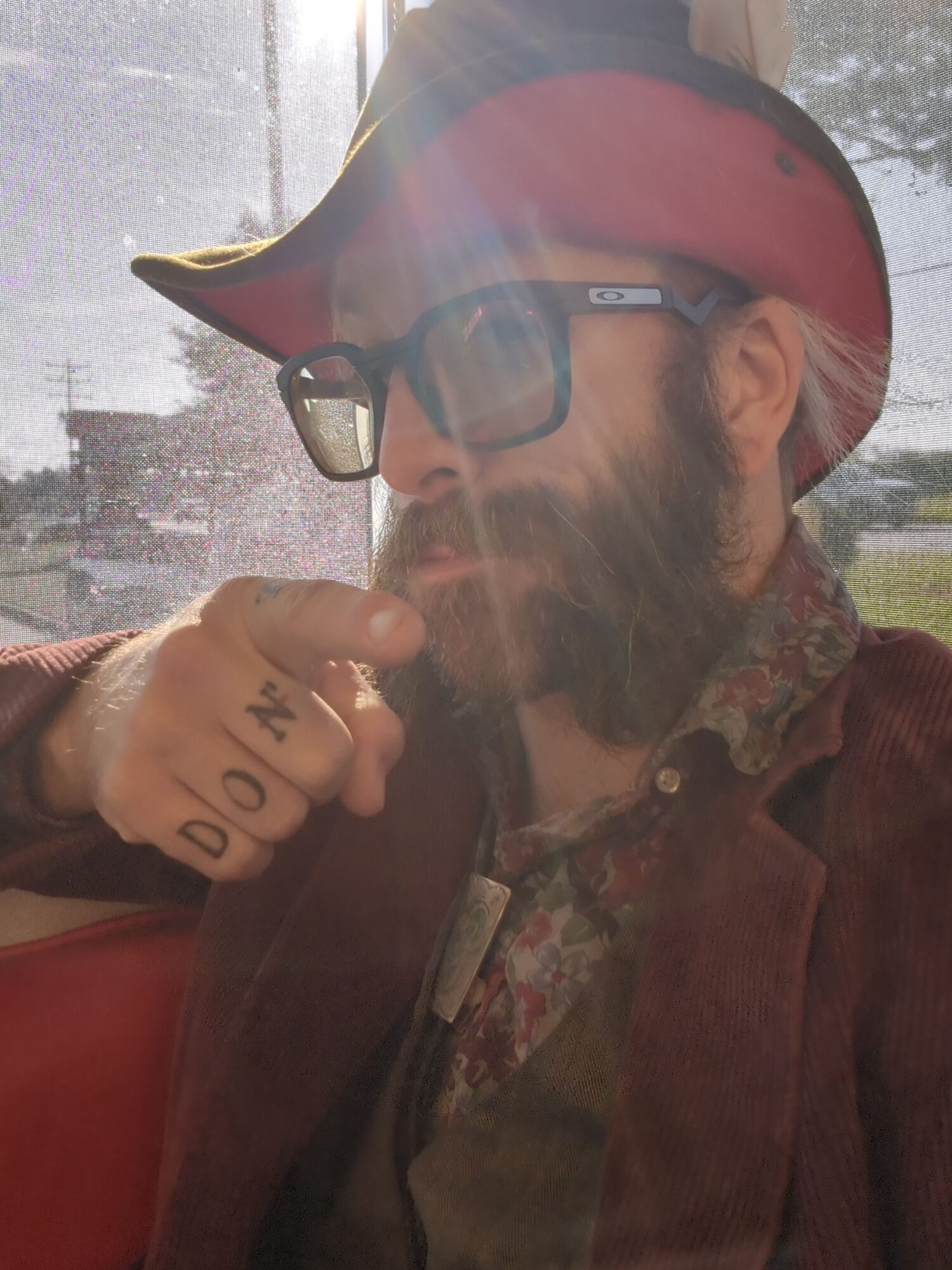 Person wearing a red helmet and glasses, holding a bag, with a window and outdoor scene in the background.