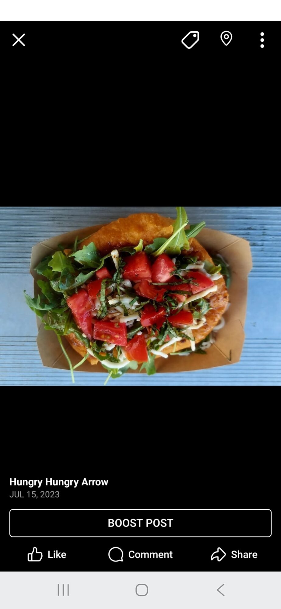 A burger with lettuce, tomato, and other ingredients in a cardboard container on a blue surface.