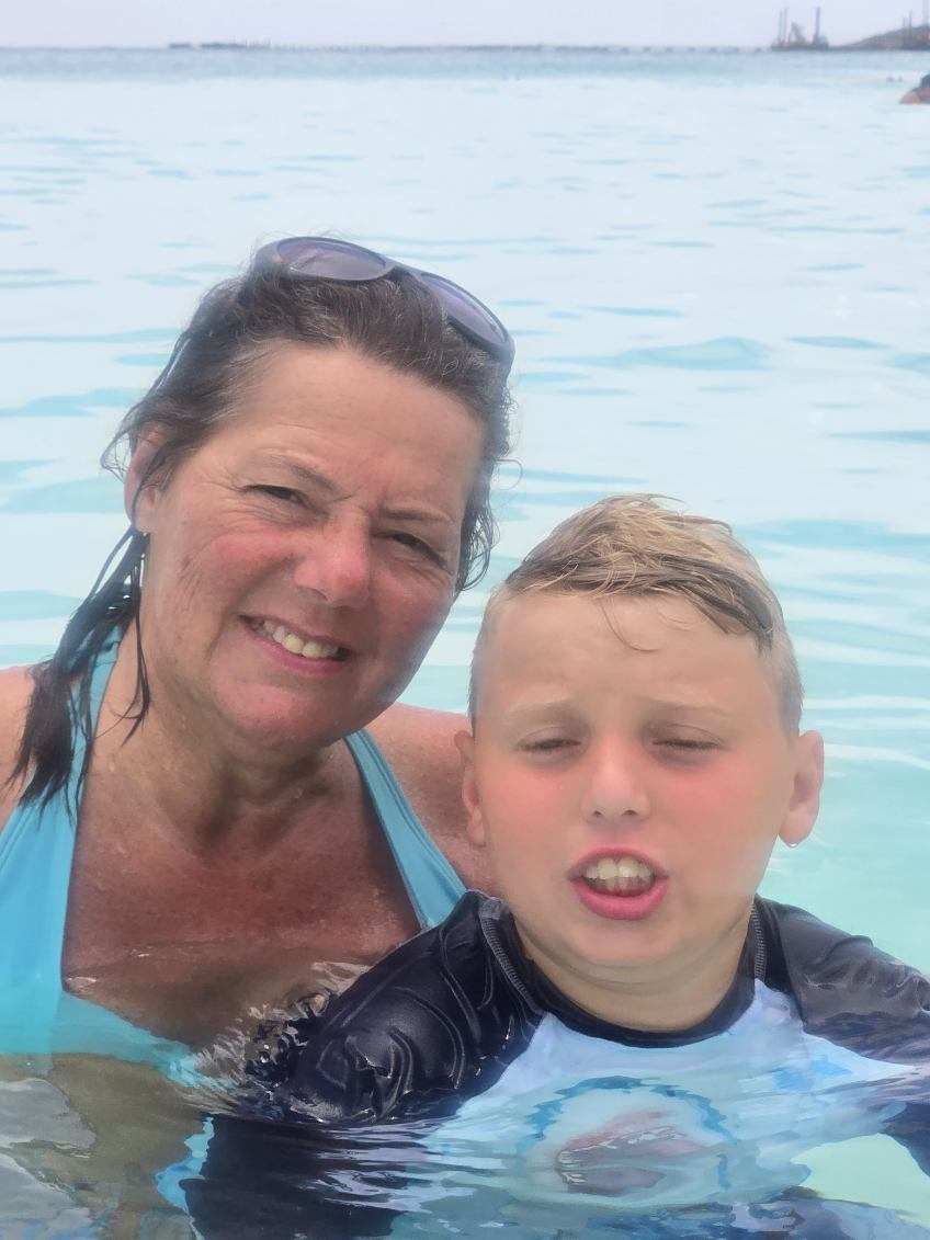 Woman and boy in water smiling at the camera, background shows water and sky.