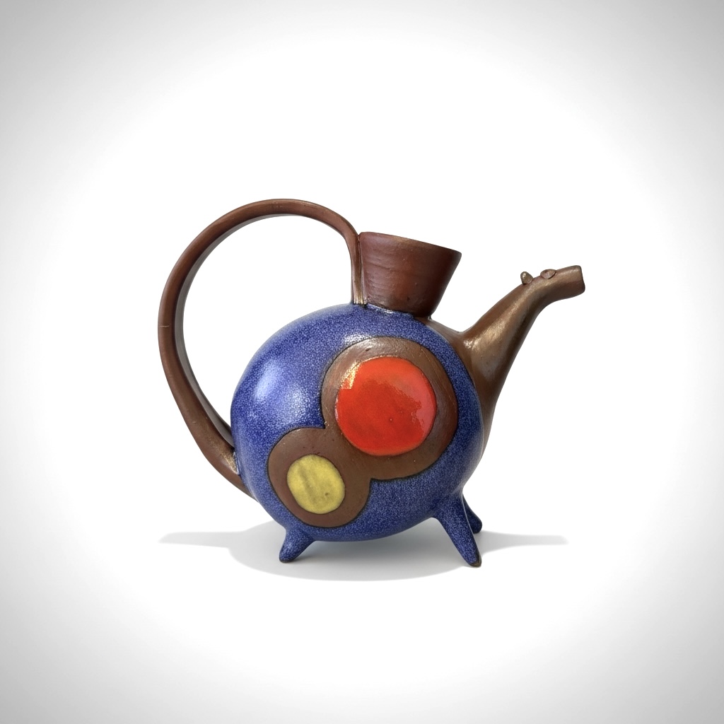 Colorful teapot designed like a whimsical creature with a round blue body, red and yellow accents, and a brown handle and spout.