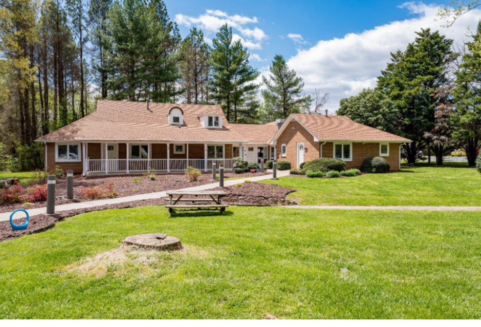 Large house with a screened porch, surrounded by trees and a well-maintained lawn, under a partly cloudy sky.