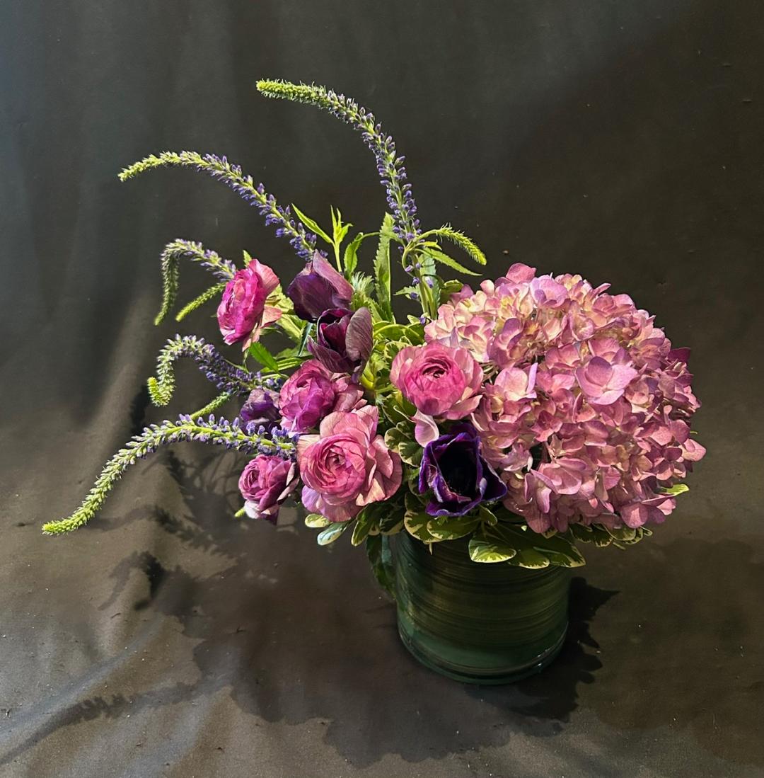 Pink and purple hydrangea and roses in a green vase, on a dark background.