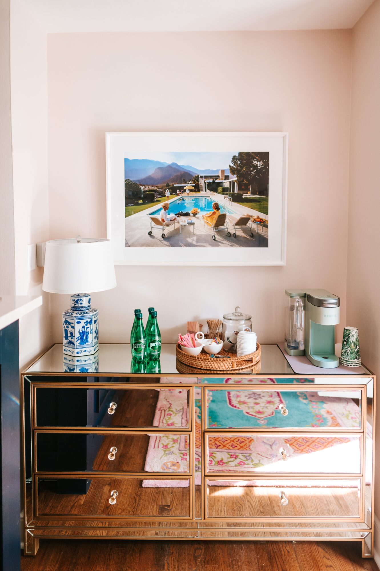 Decorative table with jars, bottles, and a lamp, with a framed landscape photo on the wall above, in a room with light-colored walls.