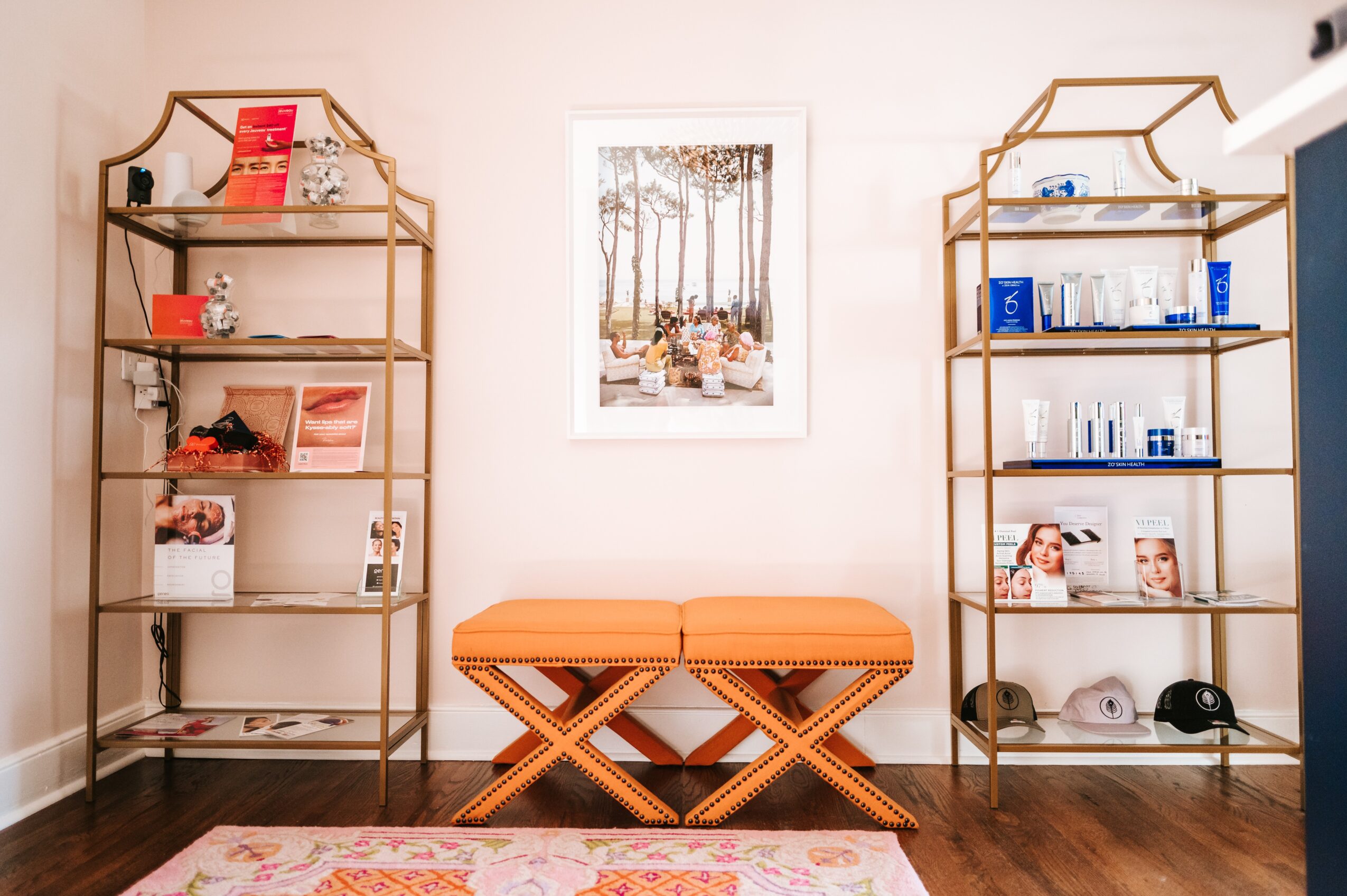Two gold-colored shelves with books and decor, a framed picture of trees, and an orange bench in a room with wooden floor.