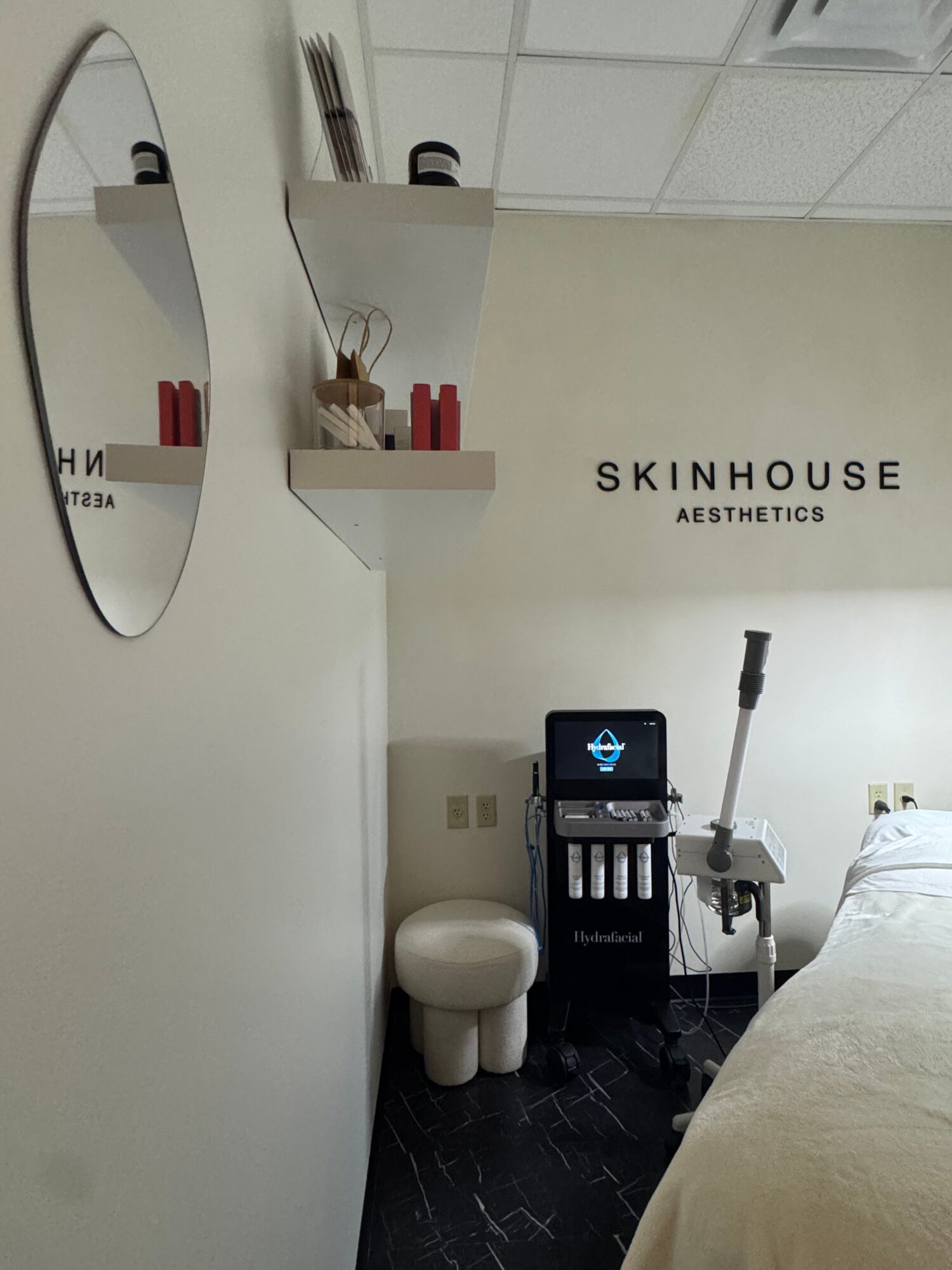 Interior of a skincare clinic with a mirror, a small shelf, and a computer monitor on a black counter.