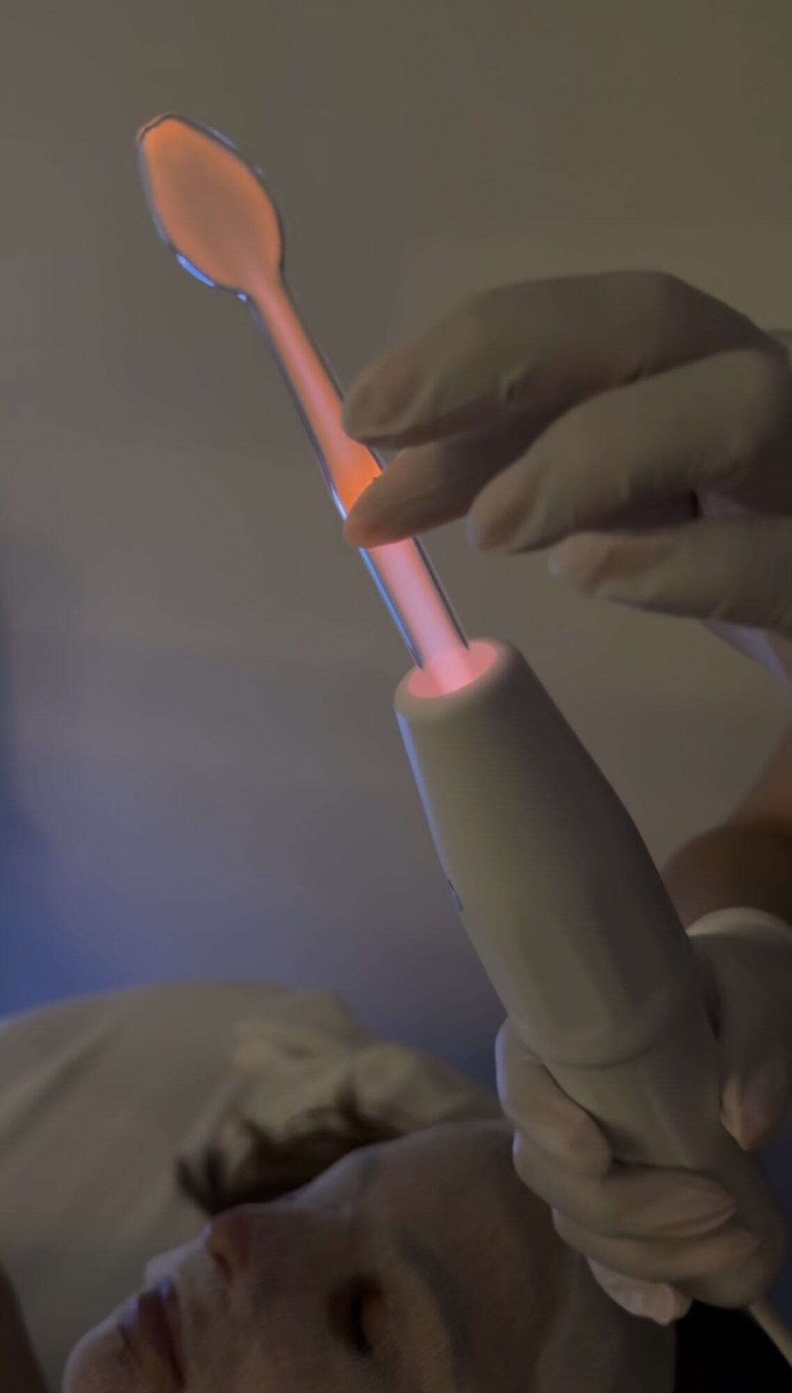 Person holding a toothbrush with a pink handle and orange brush head, near a person's face, in a dental setting.