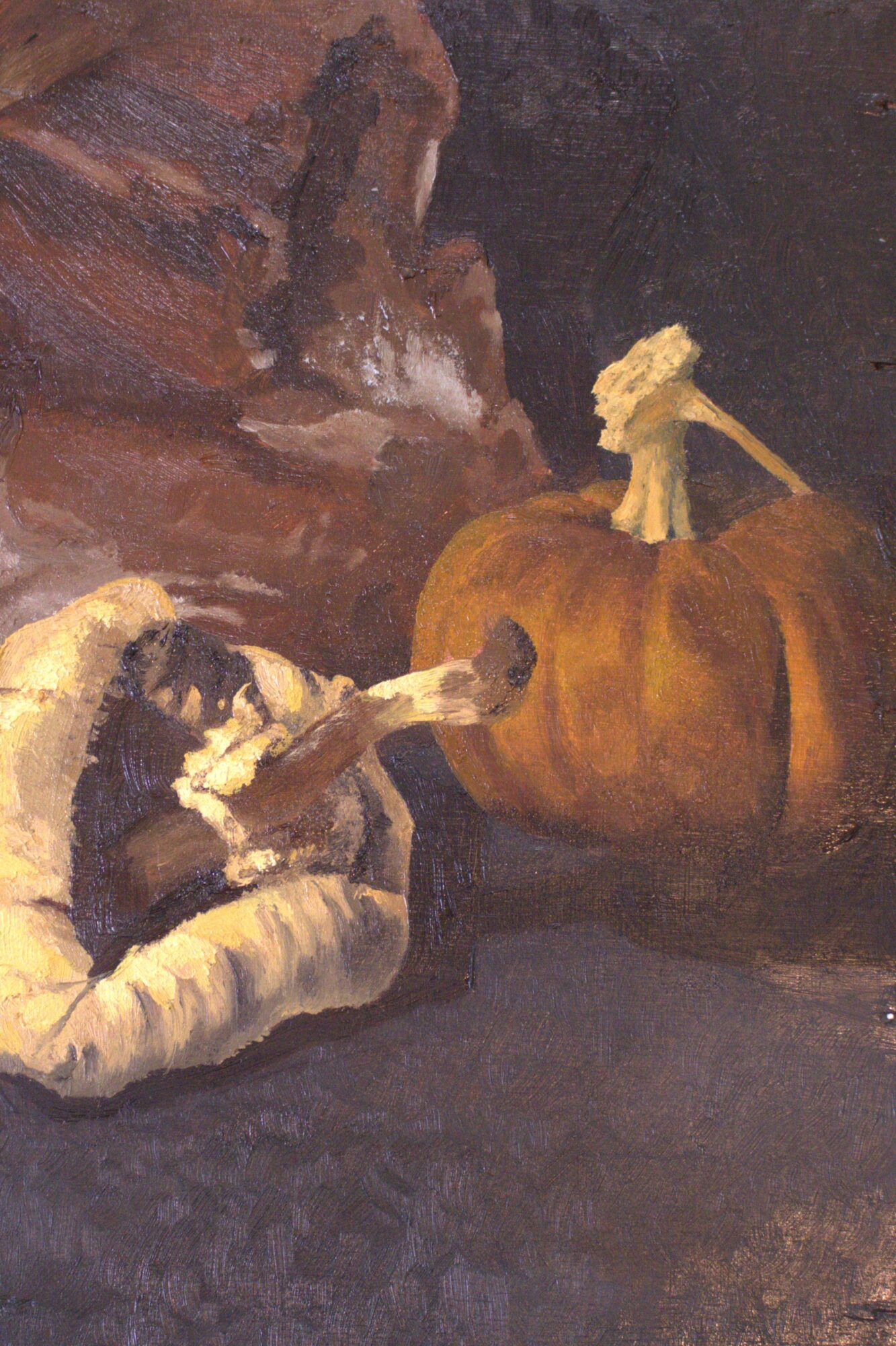A dog lying on a cushion reaches toward a large pumpkin with a stem and a small figure on top, against a dark background.