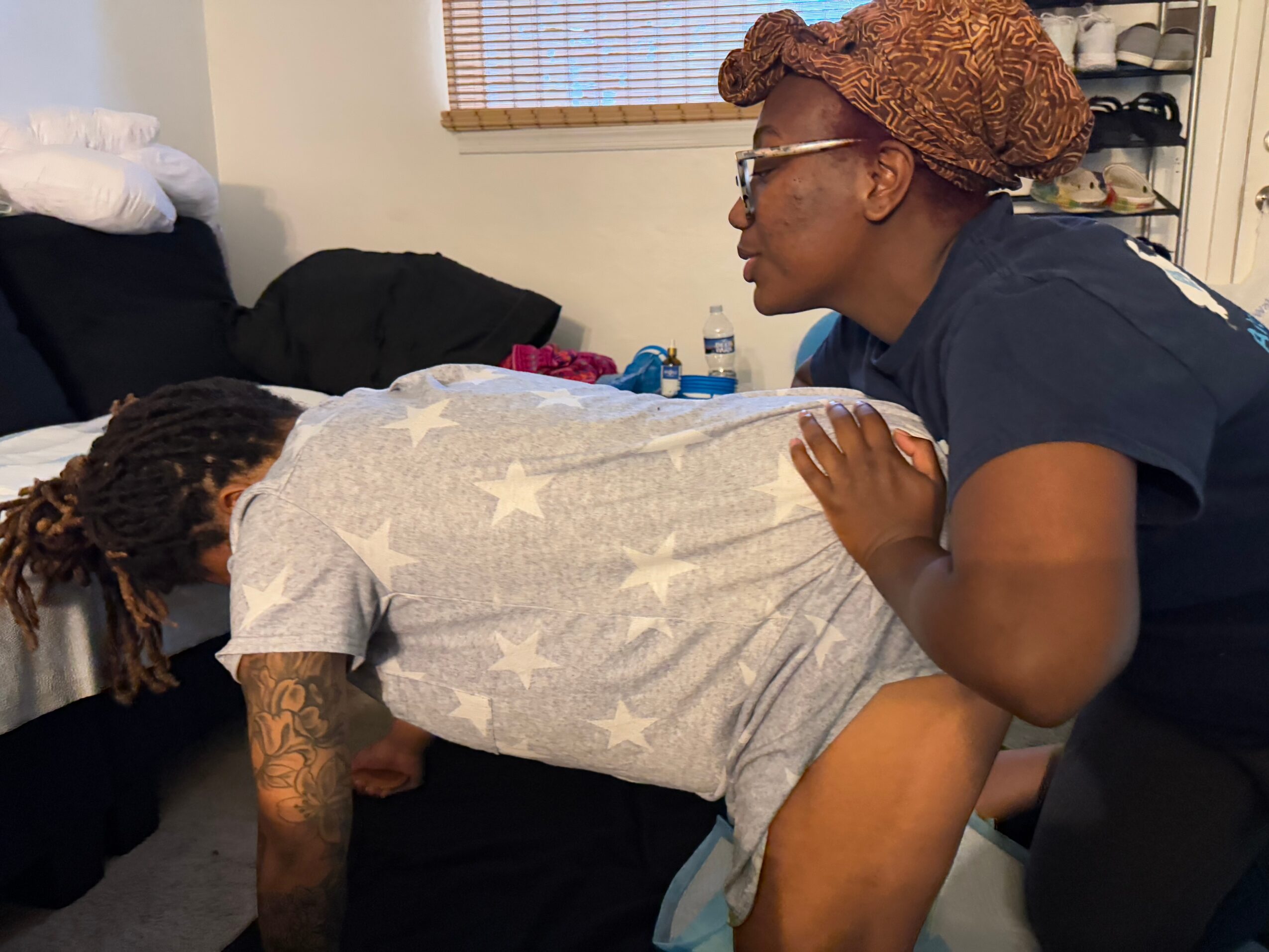 A person lying face down on a bed with a star-patterned blanket, another person leaning over them, supporting their back.