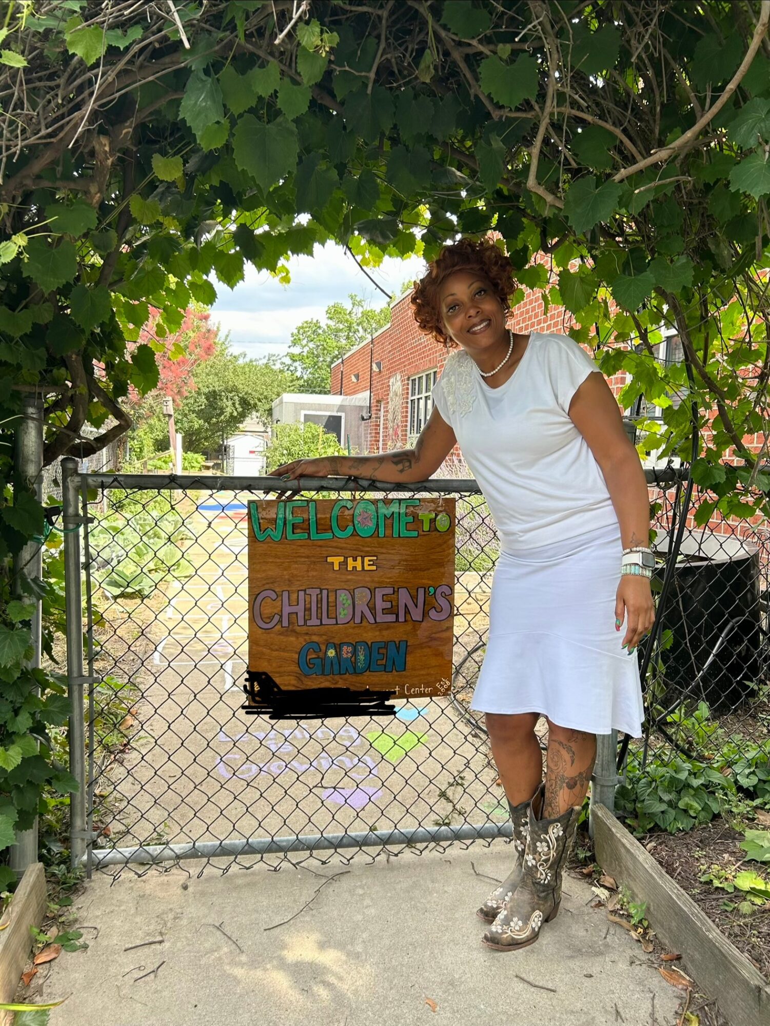 Woman in white dress standing next to a gate with a colorful sign that reads