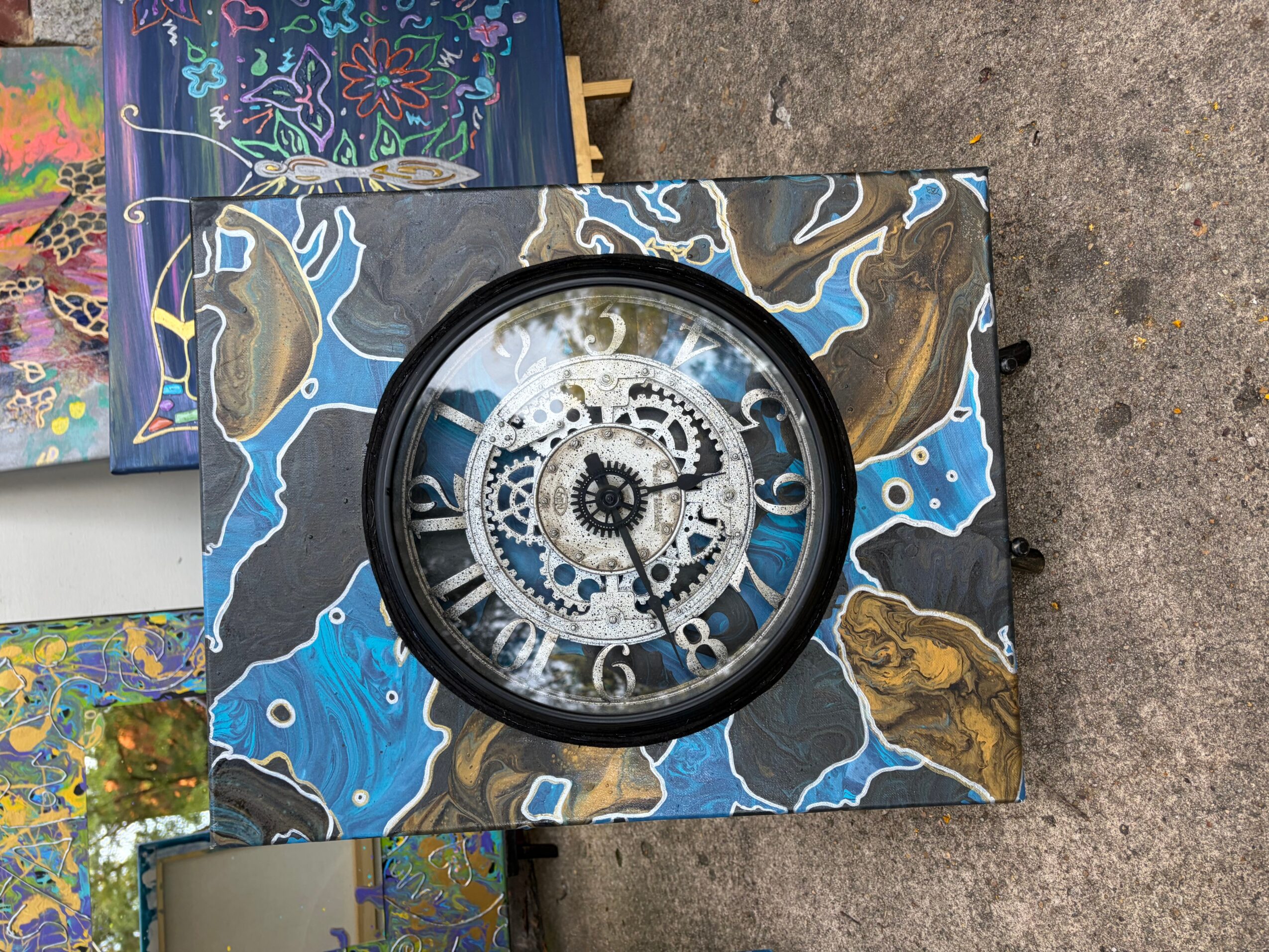 Clock with a decorative marbled frame, visible gears inside, and Roman numerals on the face.