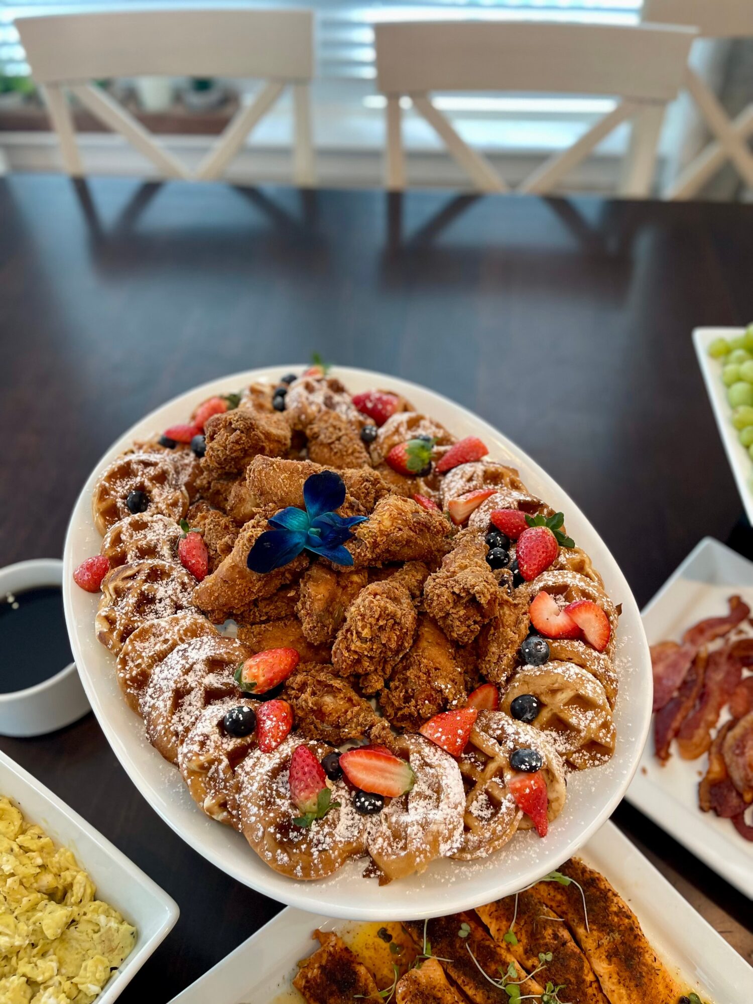 Oval platter with fried chicken pieces, strawberries, blueberries, and powdered sugar, garnished with a blue butterfly decoration.