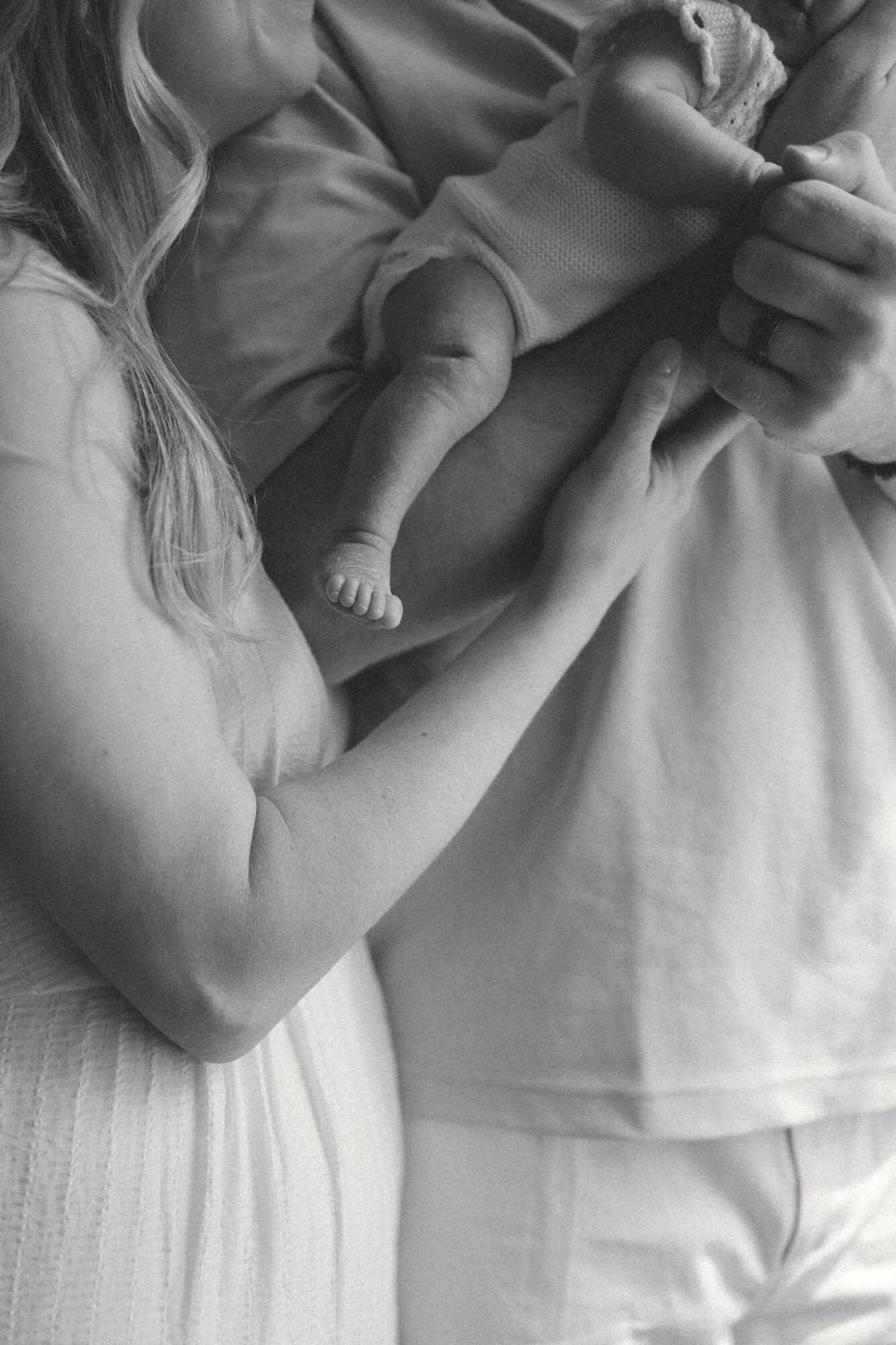 A person holds a newborn baby, with a woman supporting the baby's body and arm, in black and white.
