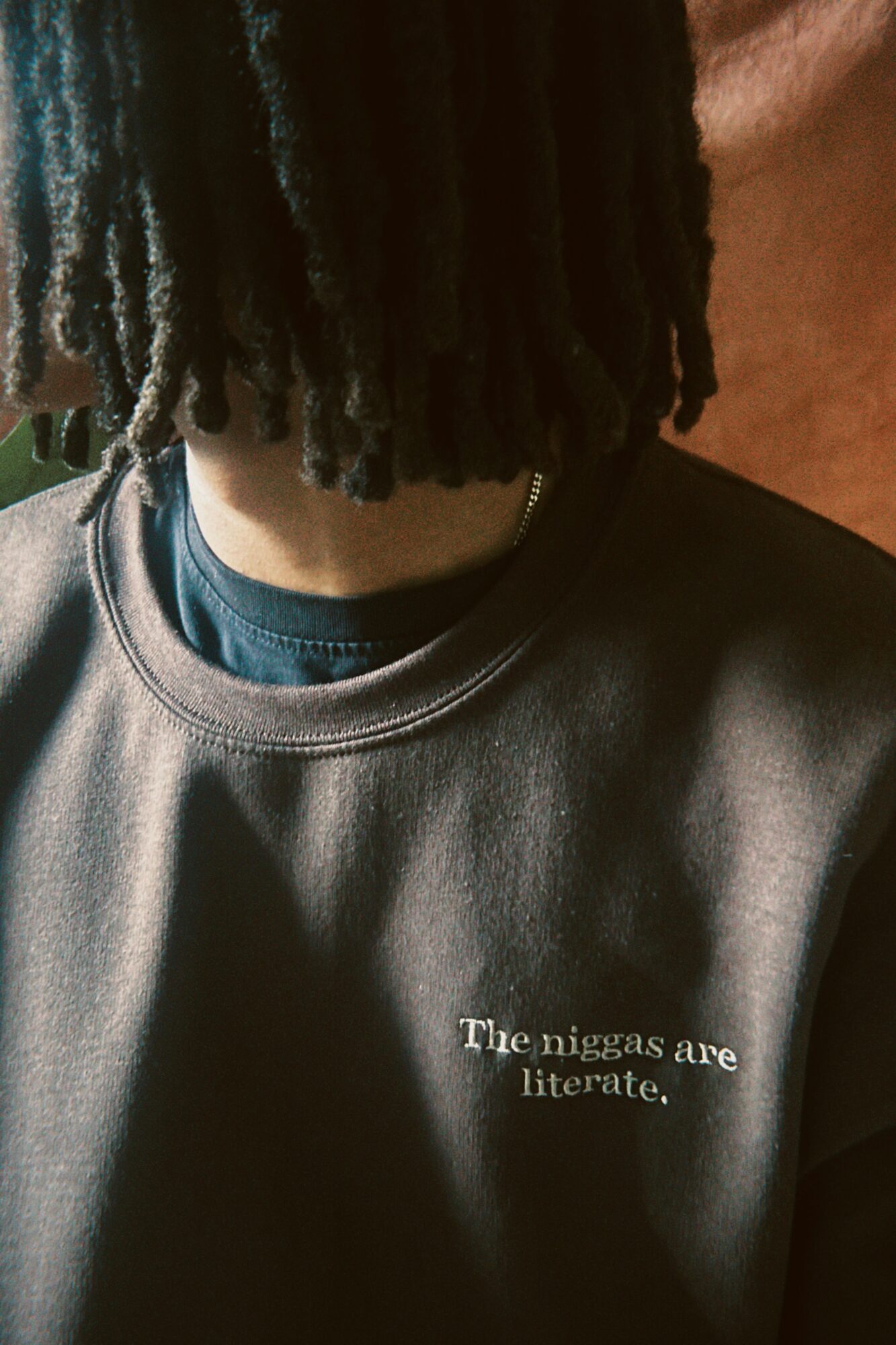 Close-up of a person with dreadlocks wearing a dark sweatshirt with text on it.