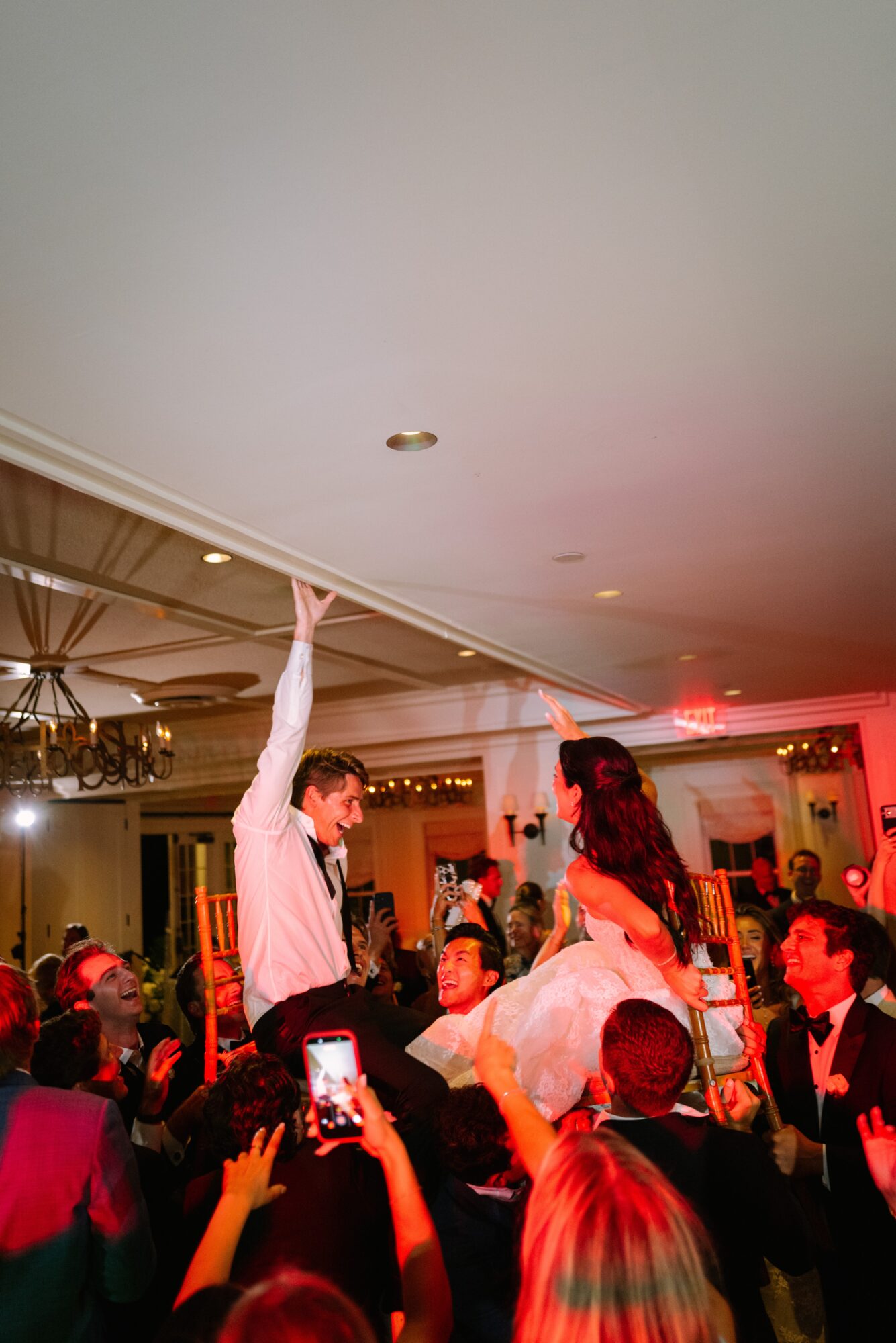 People dancing and celebrating at a party with a man and woman in the center, some taking photos, festive atmosphere.