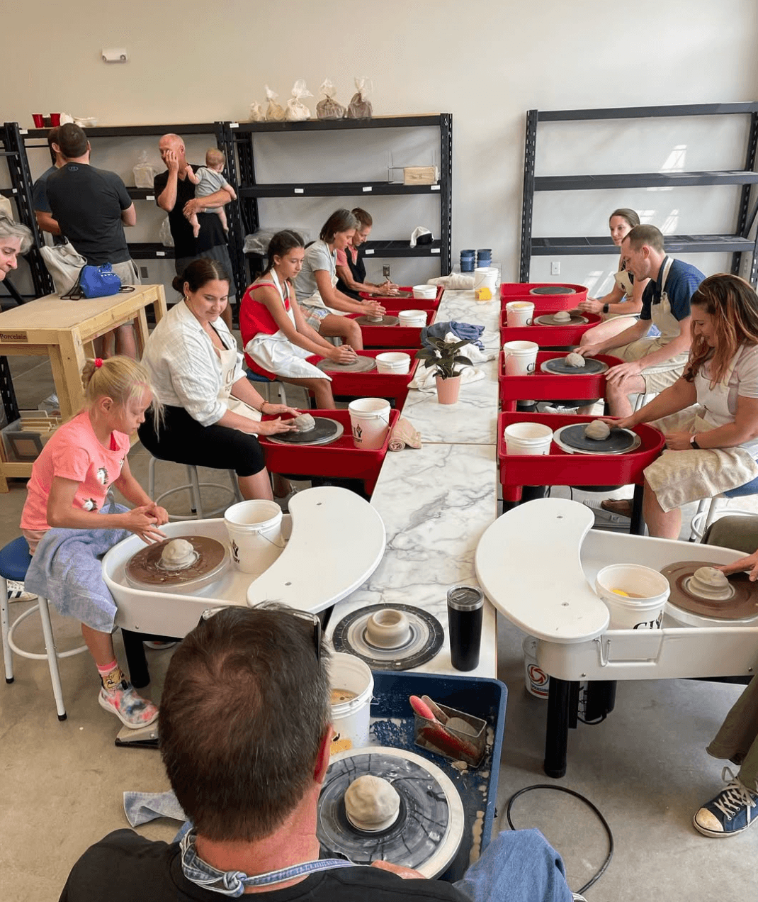 People seated at red tables in a room, preparing food or baking, with shelves and supplies in the background.